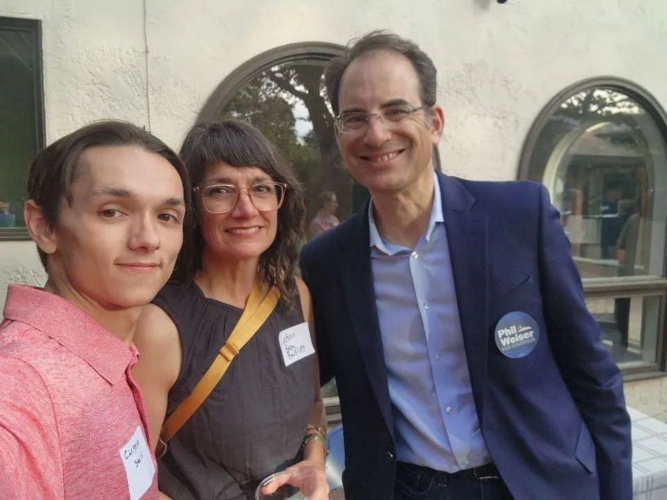 Christian Seale, candidate for El Paso County Commissioner District 5 and Phil Wisner smiling in an outdoor setting, wearing name tags, with two arched windows in the background.