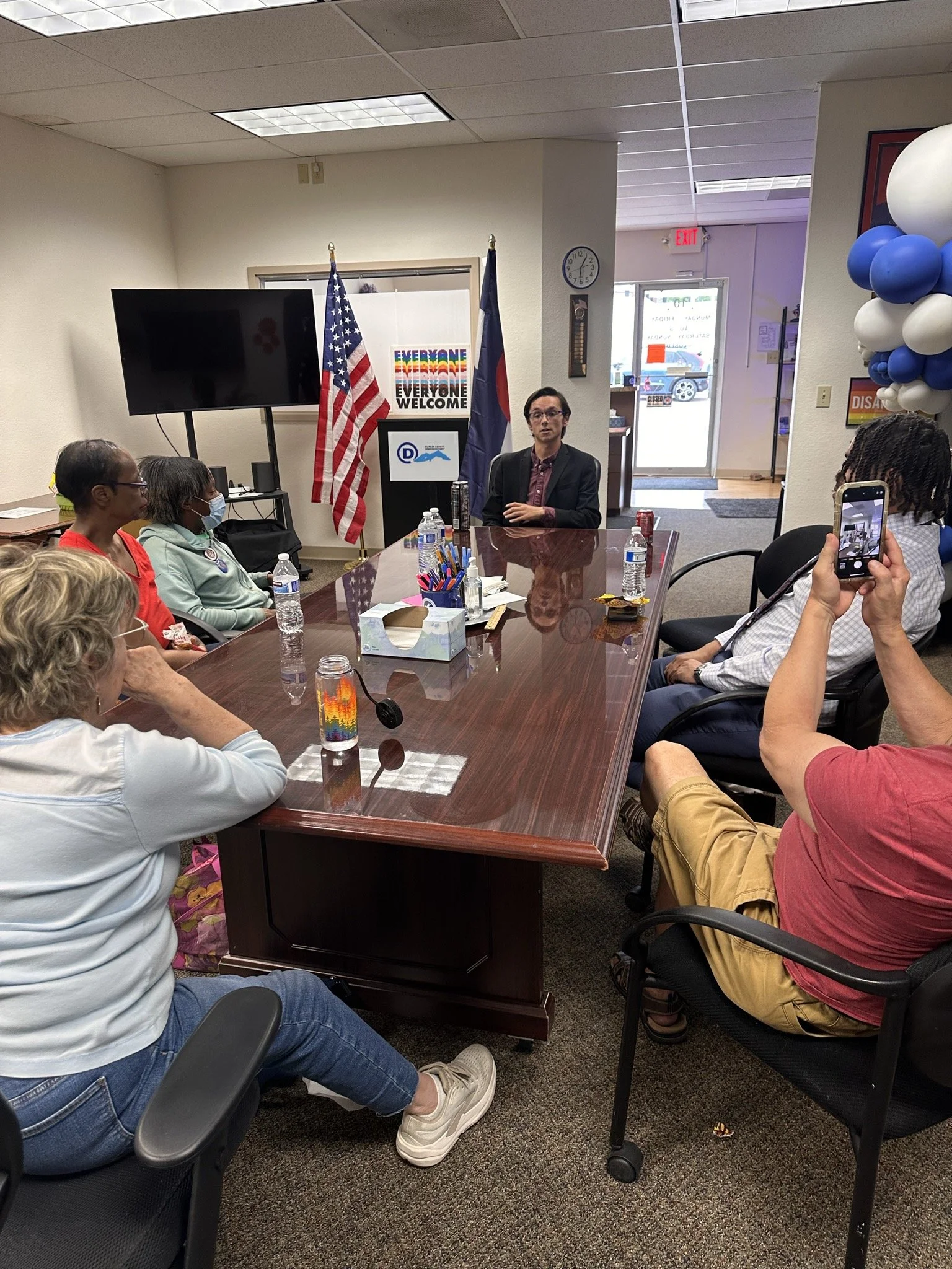 Christian Seale for County Commissioner | El Paso County District 5 at town hall sitting around a conference table in a meeting room with flags, a large screen, and posters on the wall, with a man at the head of the table speaking.