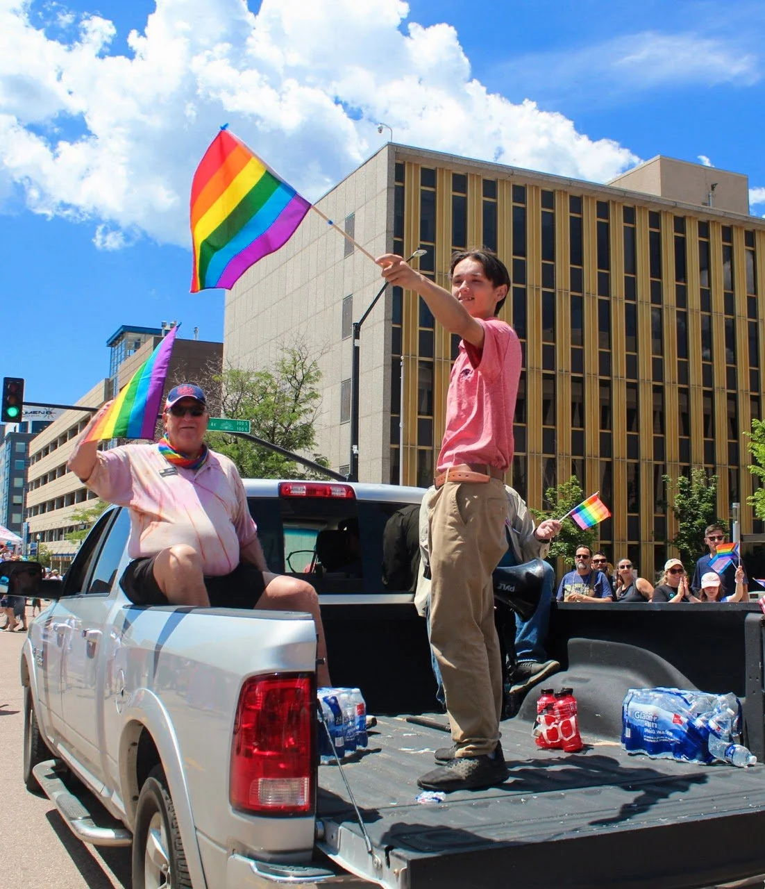 Christian Seale, candidate for El Paso County Commissioner District 5 celebrating at a pride parade, waving rainbow flags in the back of a pickup truck on city streets.