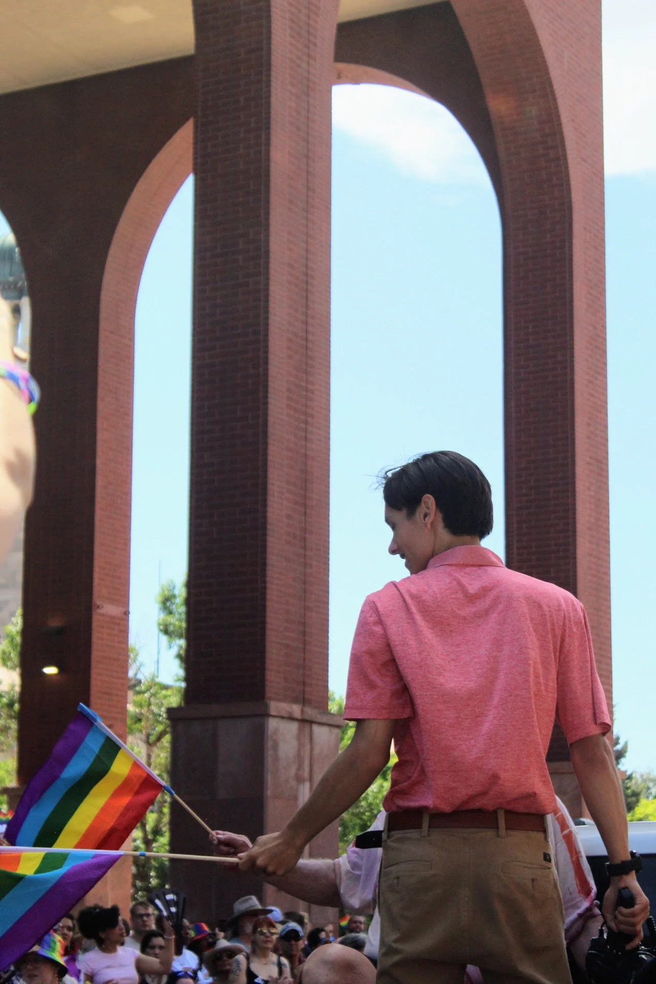 Christian Seale, candidate for El Paso County Commissioner District 5 wearing a pink shirt holding a rainbow pride flag at a gathering or pride event.