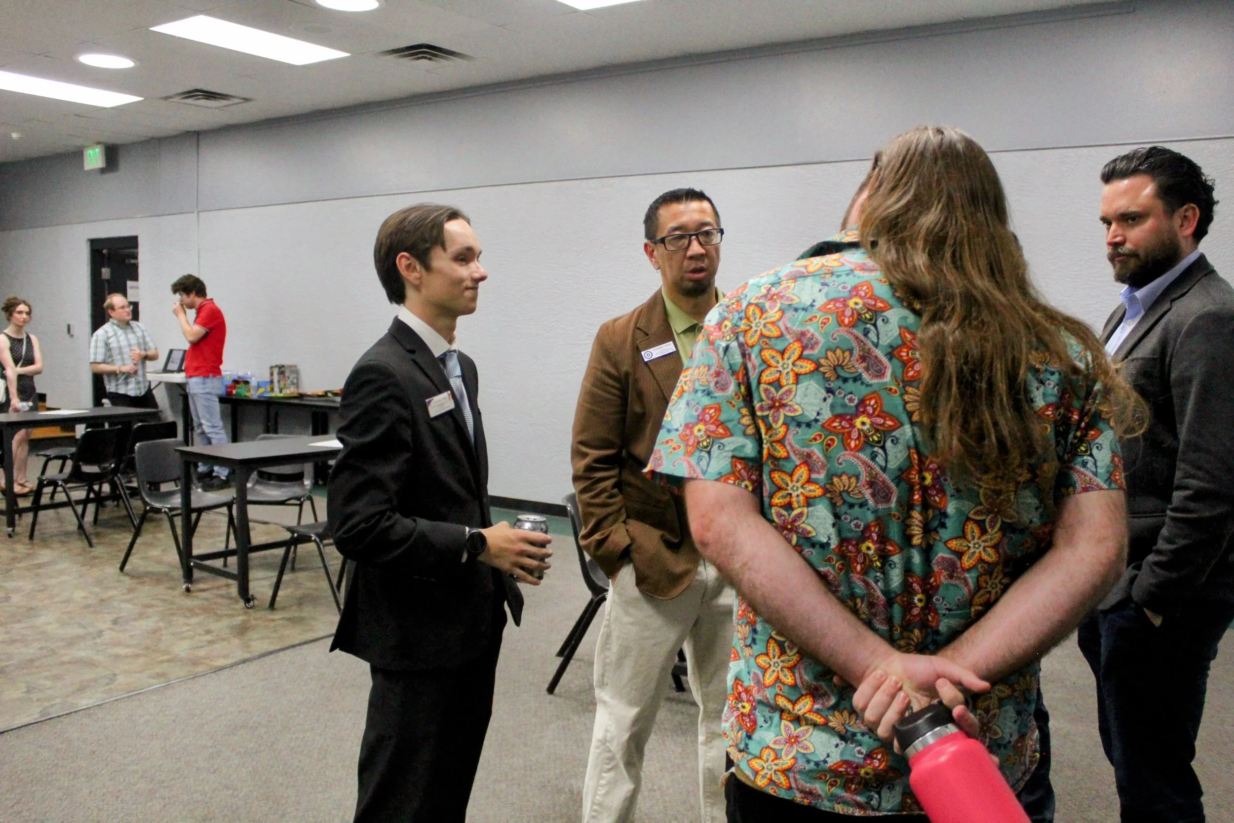 Group of people engaged in conversation with Christian Seale, candidate for El Paso County Commissioner District 5 at a professional event or conference in a room with tables and chairs.