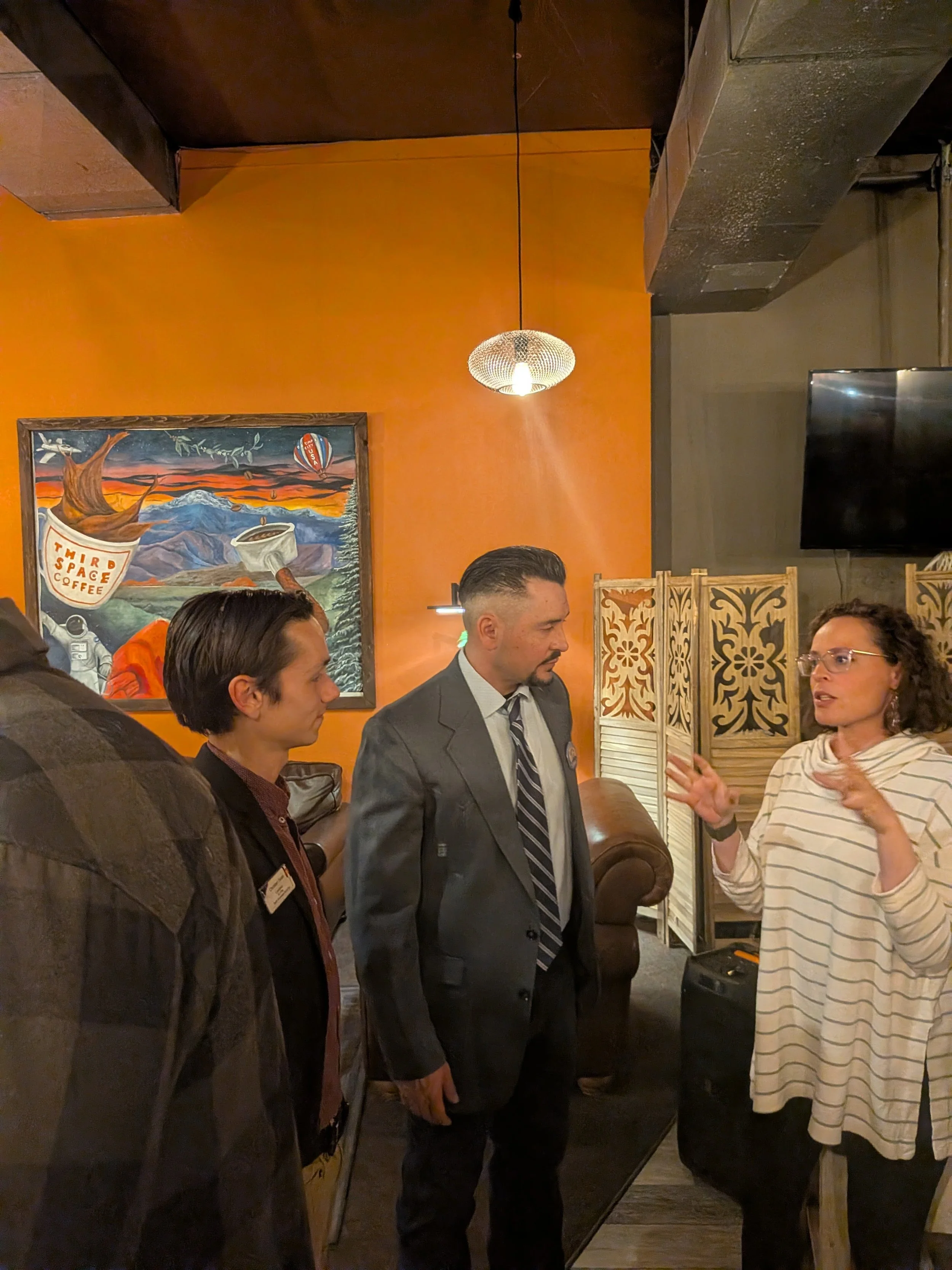 A woman is speaking to Christian Seale for County Commissioner District 5 in a dimly lit room with orange walls, a painting, and a TV in the background.