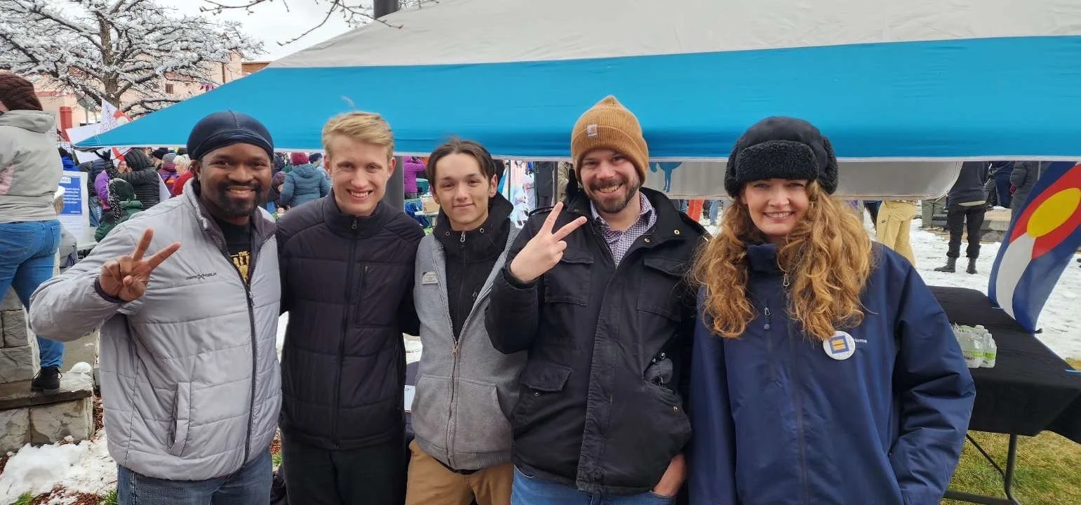 Christian Seale, candidate for El Paso County Commissioner District 5 and others smiling and posing in front of a canopy at an outdoor event on a snowy day, some making peace signs.