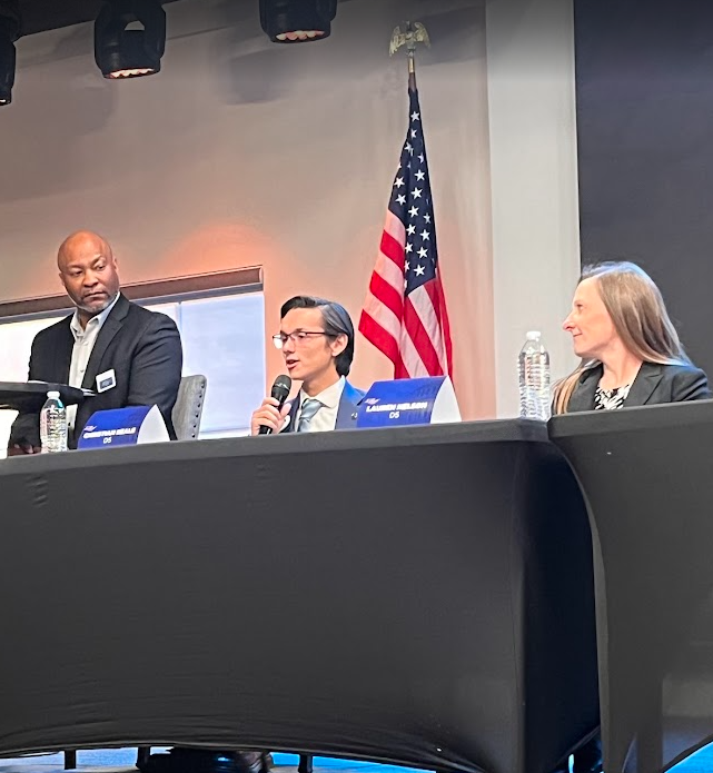 Christian Seale for County Commissioner | El Paso County District 5 at at Chruch of all Nation County Commissioner Froum sitting at a table with an American flag in the background. The person in the middle is speaking into a microphone, while the oth