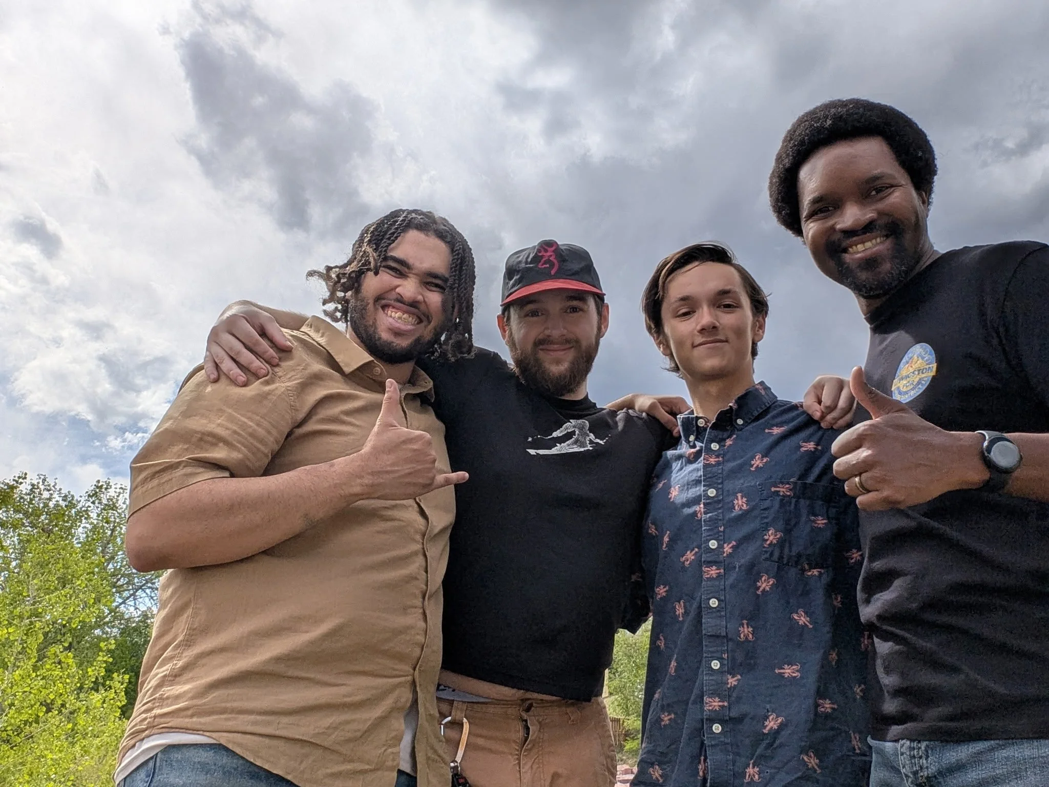 Christian Seale for County Commissioner | El Paso County District 5 and 4 men smiling and posing together outdoors under cloudy sky, some with arms around each other, in a park-like setting with trees. Sand Creek Trail Cleanup