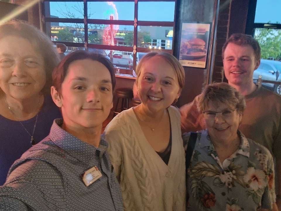 Group of five people including Christian Seale, candidate for El Paso County Commissioner District 5 smiling in a restaurant or bar with large windows and neon signs outside.