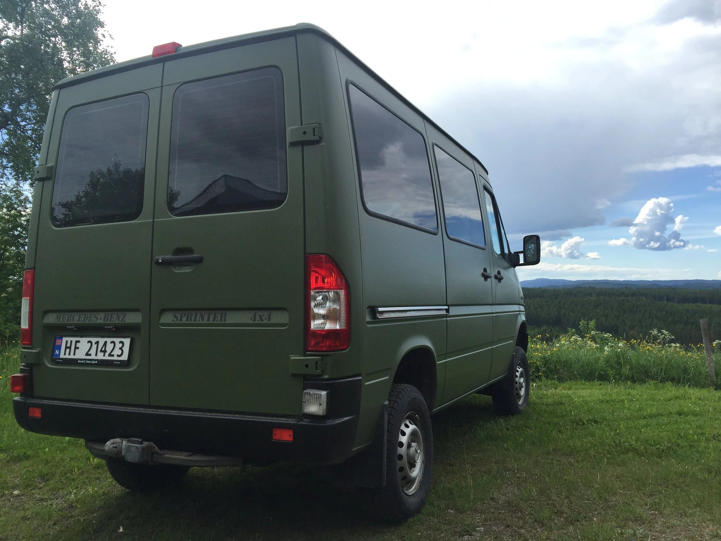 The PhotoVan parked on grass with a scenic view of fields, trees, and a cloudy sky in the background.