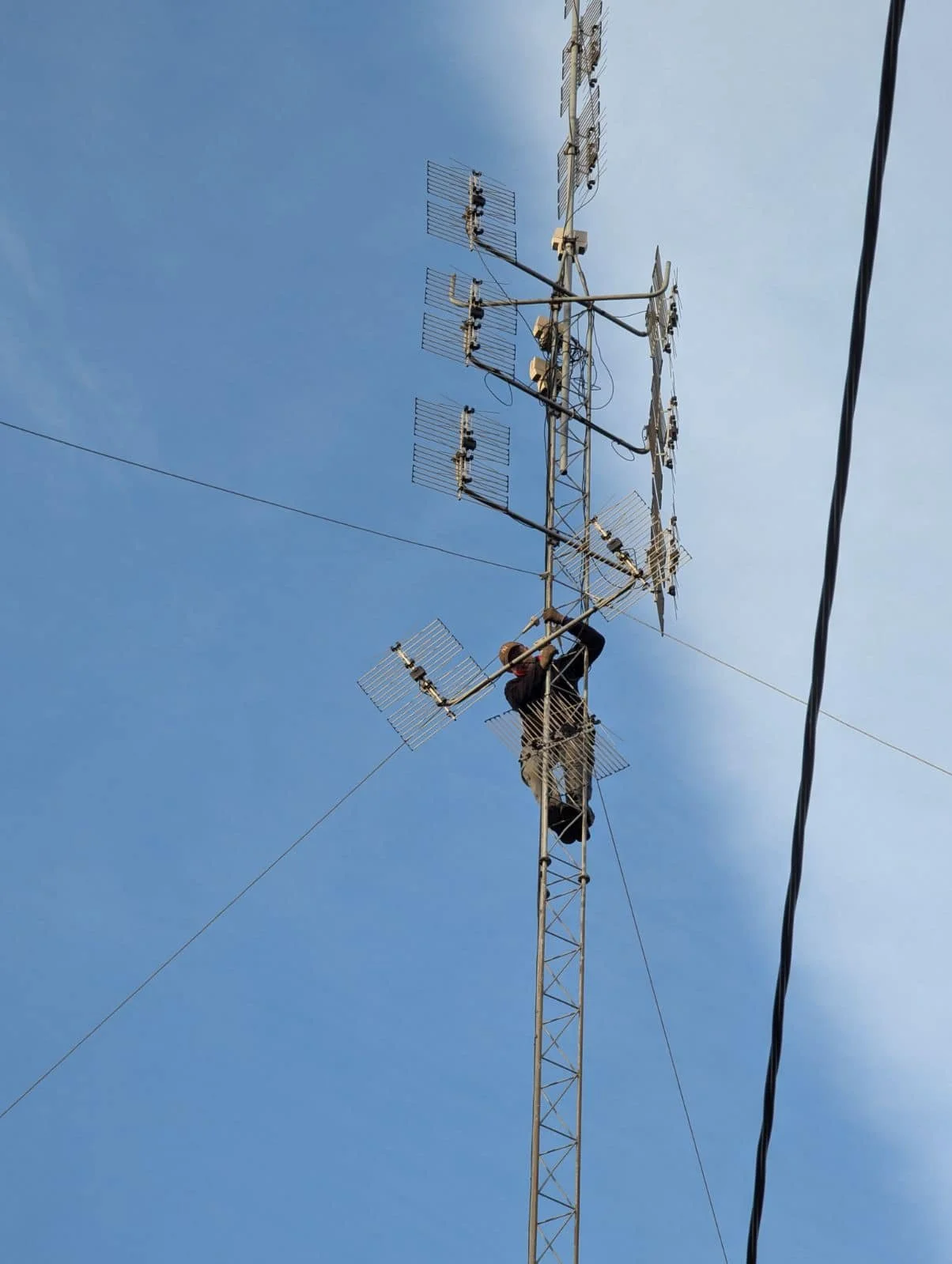 Svenn Erik Høylie is working on a radio tower with multiple antennas against a blue sky.