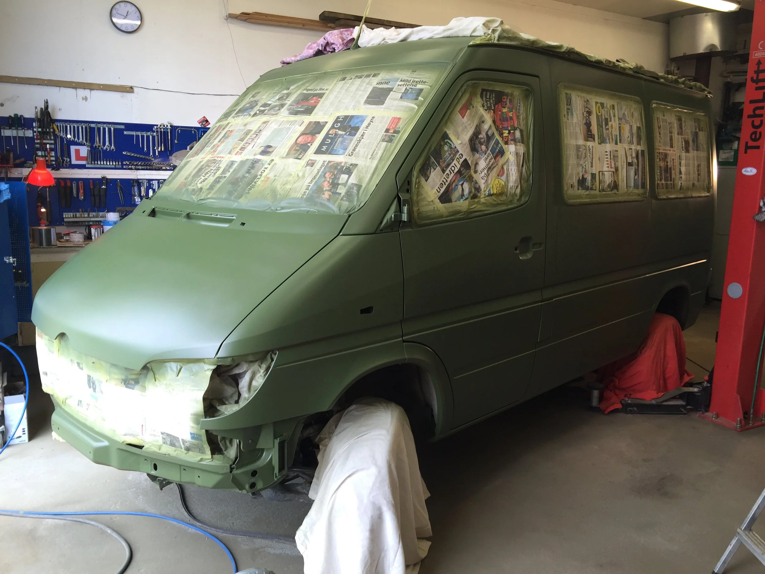 The PhotoVan being painted in a garage, with the body painted matte green and covered partially with newspaper and masking tape for detailing.