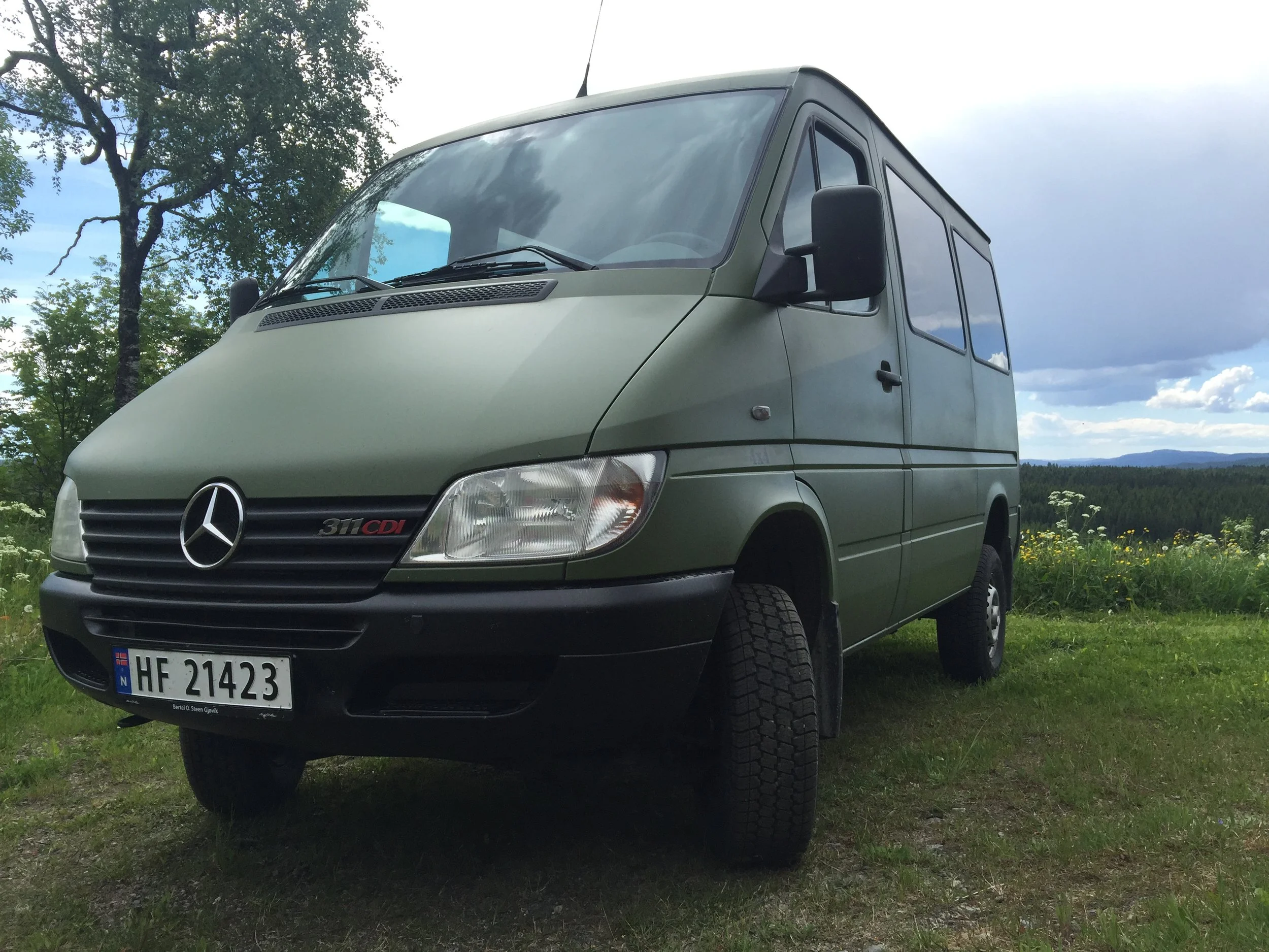 The PhotoVan parked on grass with trees and a cloudy sky in the background.