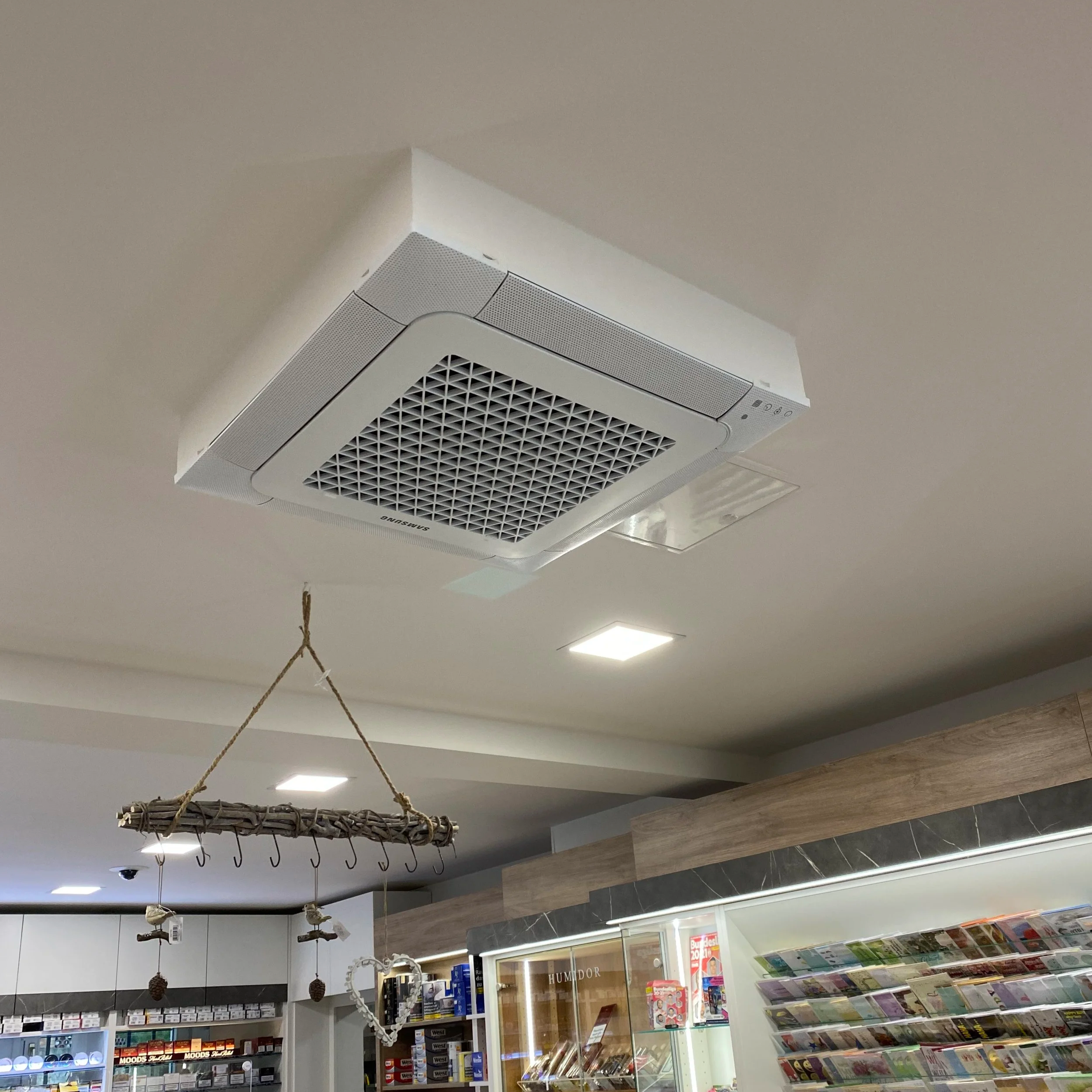 Innenaufnahme eines Lebensmittelgeschäfts mit Klimaanlagen, Beleuchtung, Regalen mit Produkten und einer hölzernen Dekoration an der Decke.