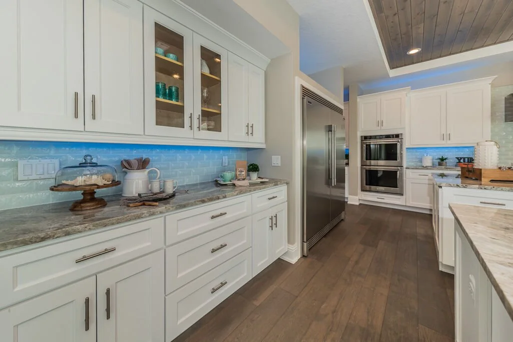 This kitchen shows how a long cabinet run can still feel light and intentional.

Glass wall cabinets, reflective backsplash, and undercabinet lighting help break up the mass of cabinetry and add more depth to the overall design. The result is a space