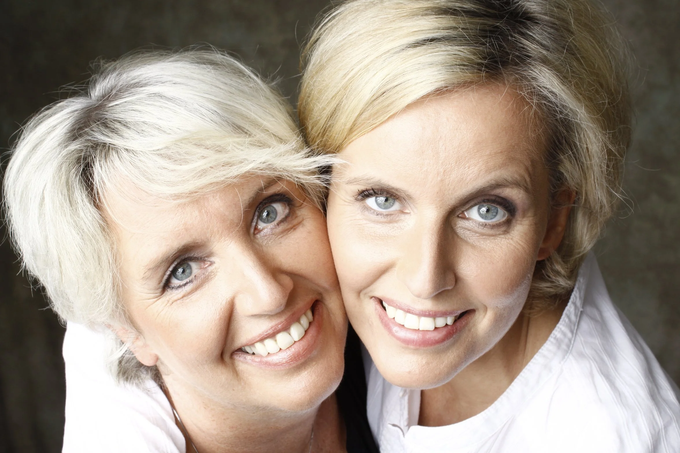 Ein lachendes älteres Frau und eine jüngere Frau, die eng zusammenstehen und die Kamera ansehen.