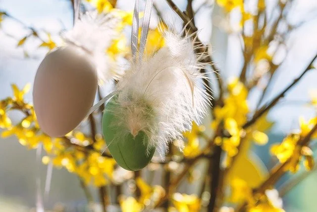 Osterdeko mit bemalter Eierschale, Federn und gelben Blüten im Hintergrund