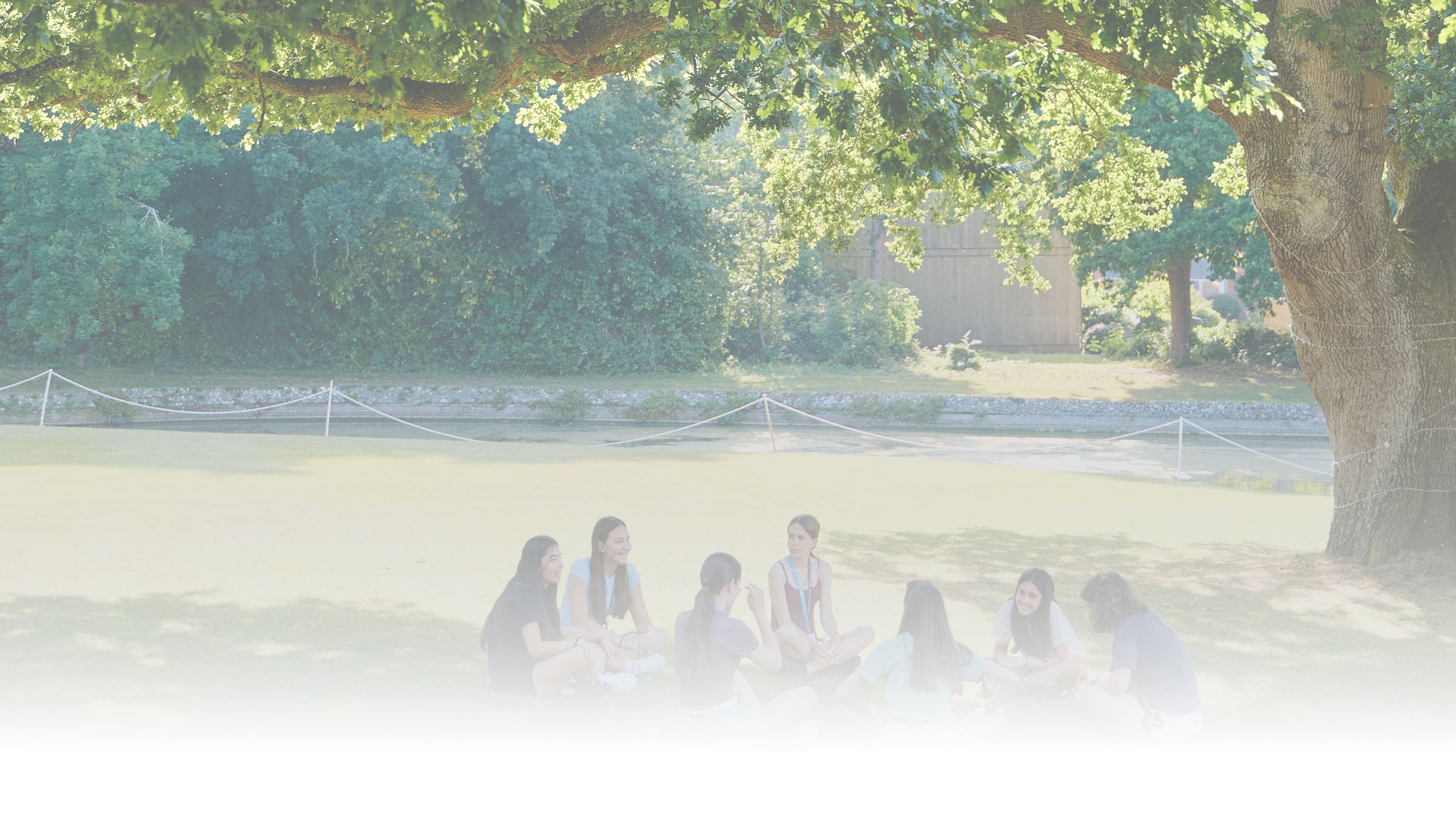 Grupo de estudiantes sentados en círculo sobre el césped, bajo un árbol, en el campus de Dicker.