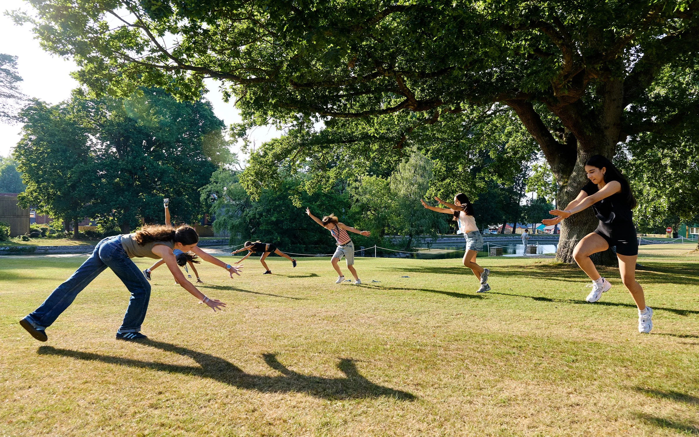 Estudiantes participando en una actividad de movimiento sobre el césped, junto a un gran árbol del campus de Dicker.