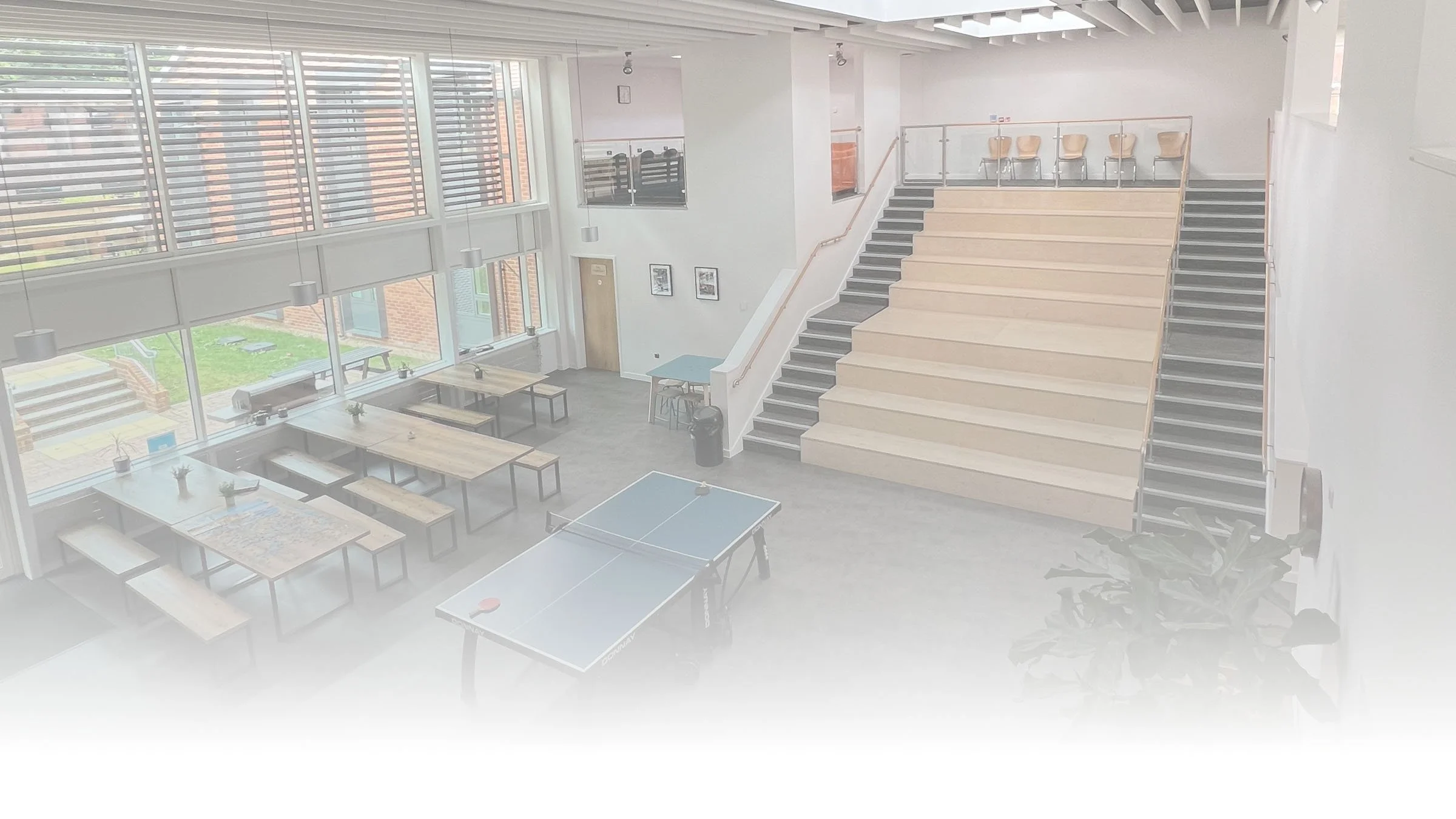 Zona común del campus de Dicker con mesas, bancos, mesa de ping-pong y asientos escalonados.