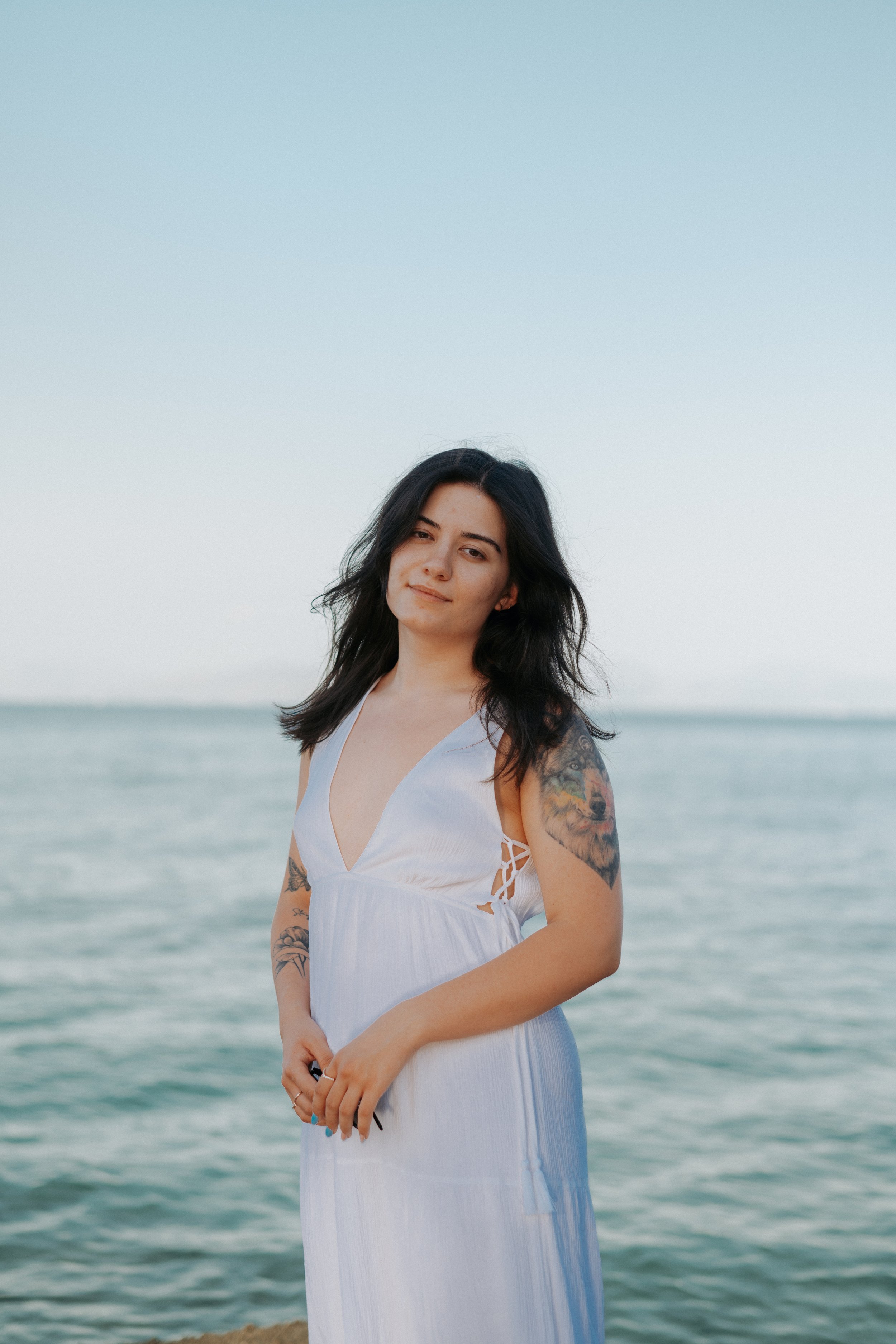 Woman in white dress with tattoos standing by the sea