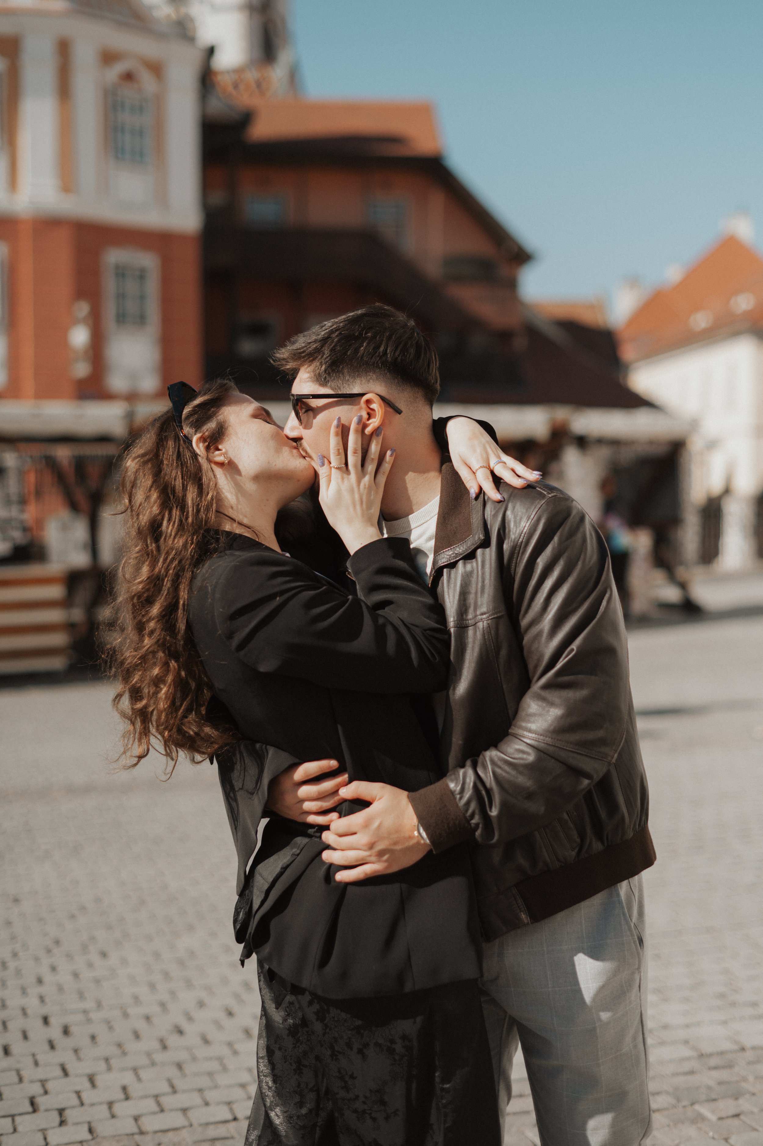 A couple kissing outdoors with historic buildings in the background.