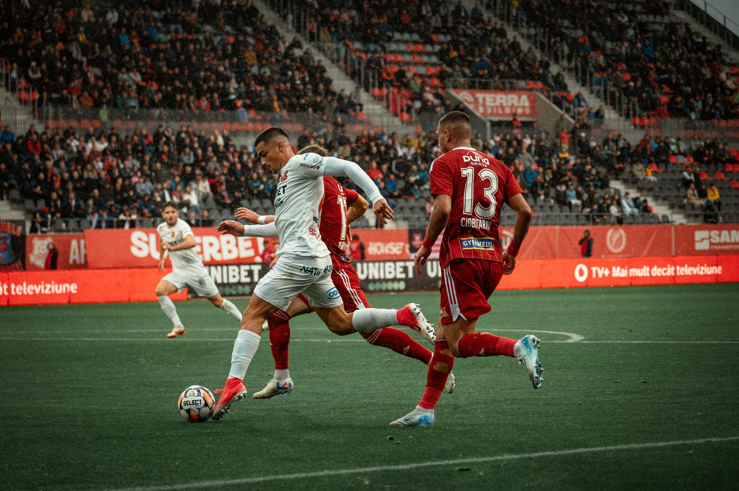 Soccer players in action during a match with a stadium audience in the background.