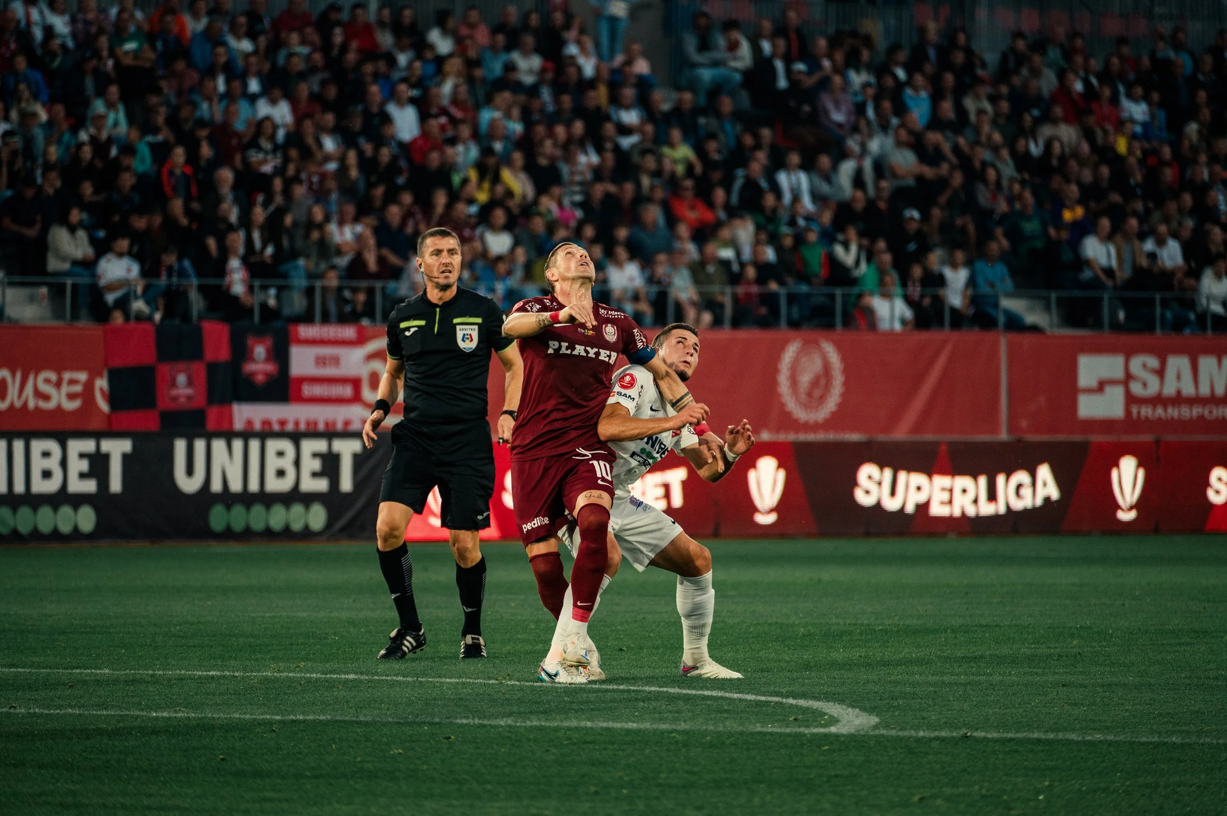 Soccer match with two players and a referee, crowded stadium background.