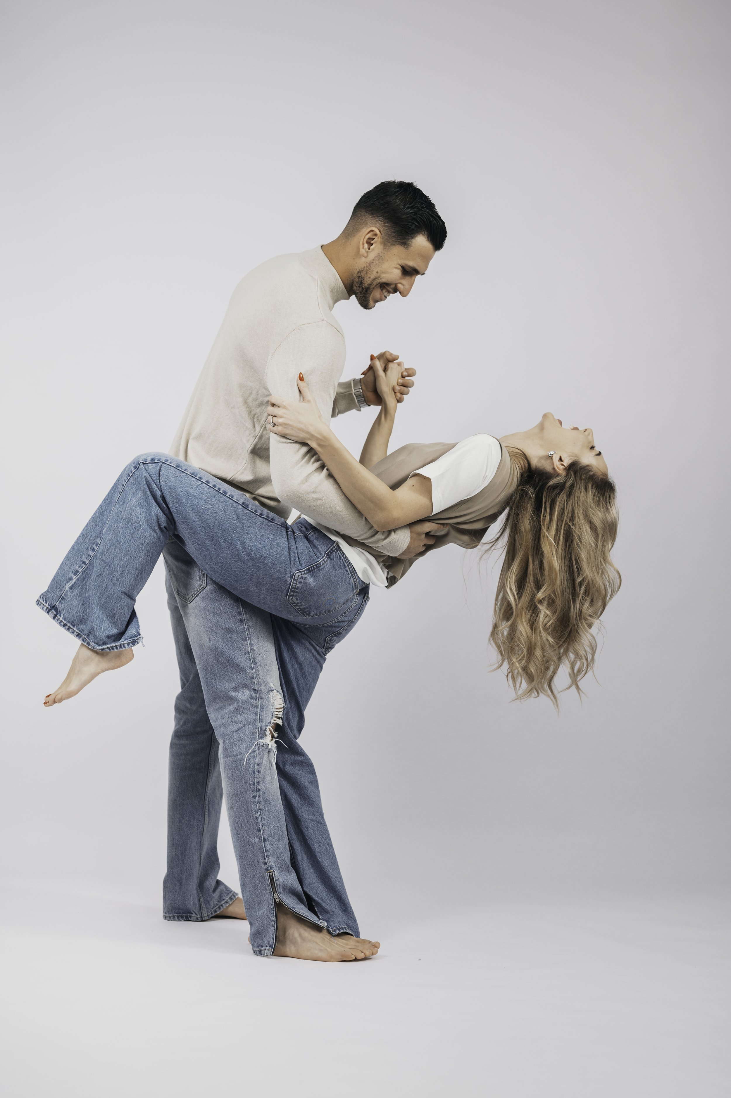 A man and woman dancing, the man holds and dips the woman, both wearing casual jeans, with a white background.
