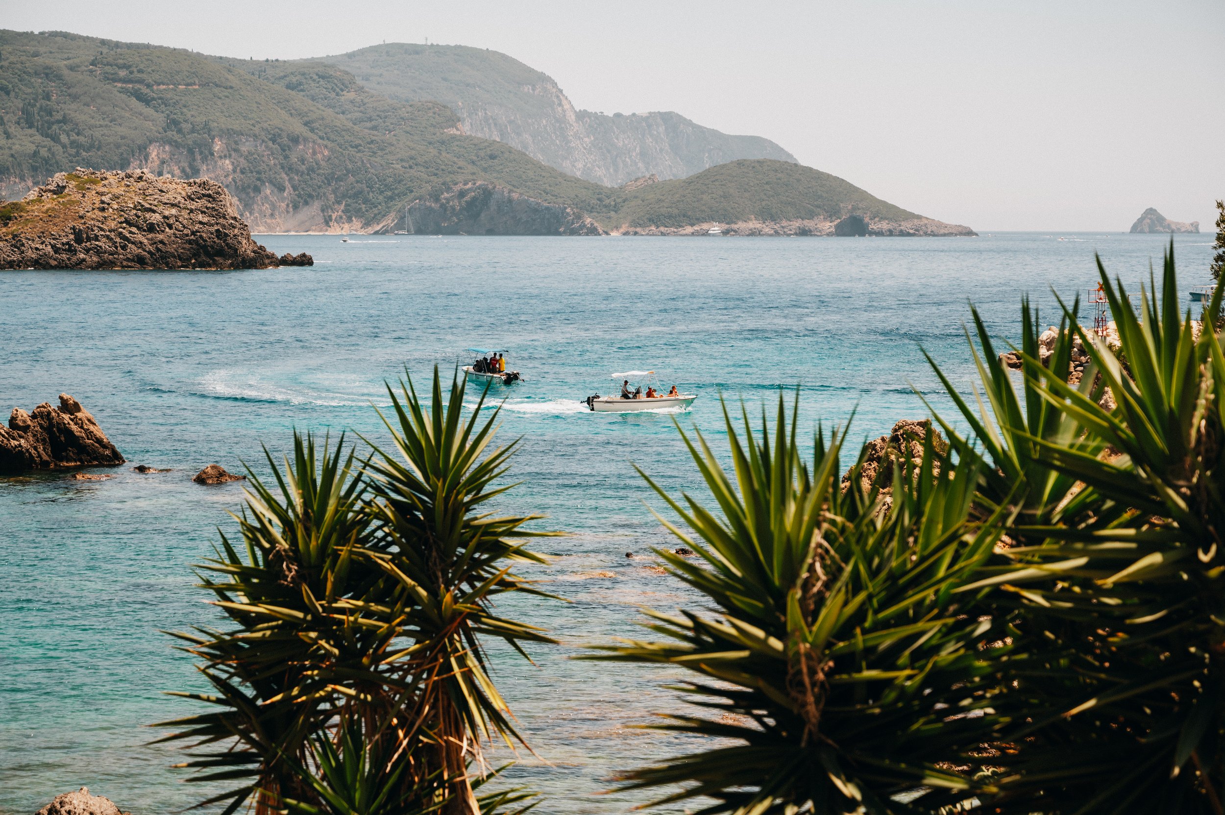 Two boats on a clear blue sea surrounded by rocky hills and lush vegetation under a sunny sky.