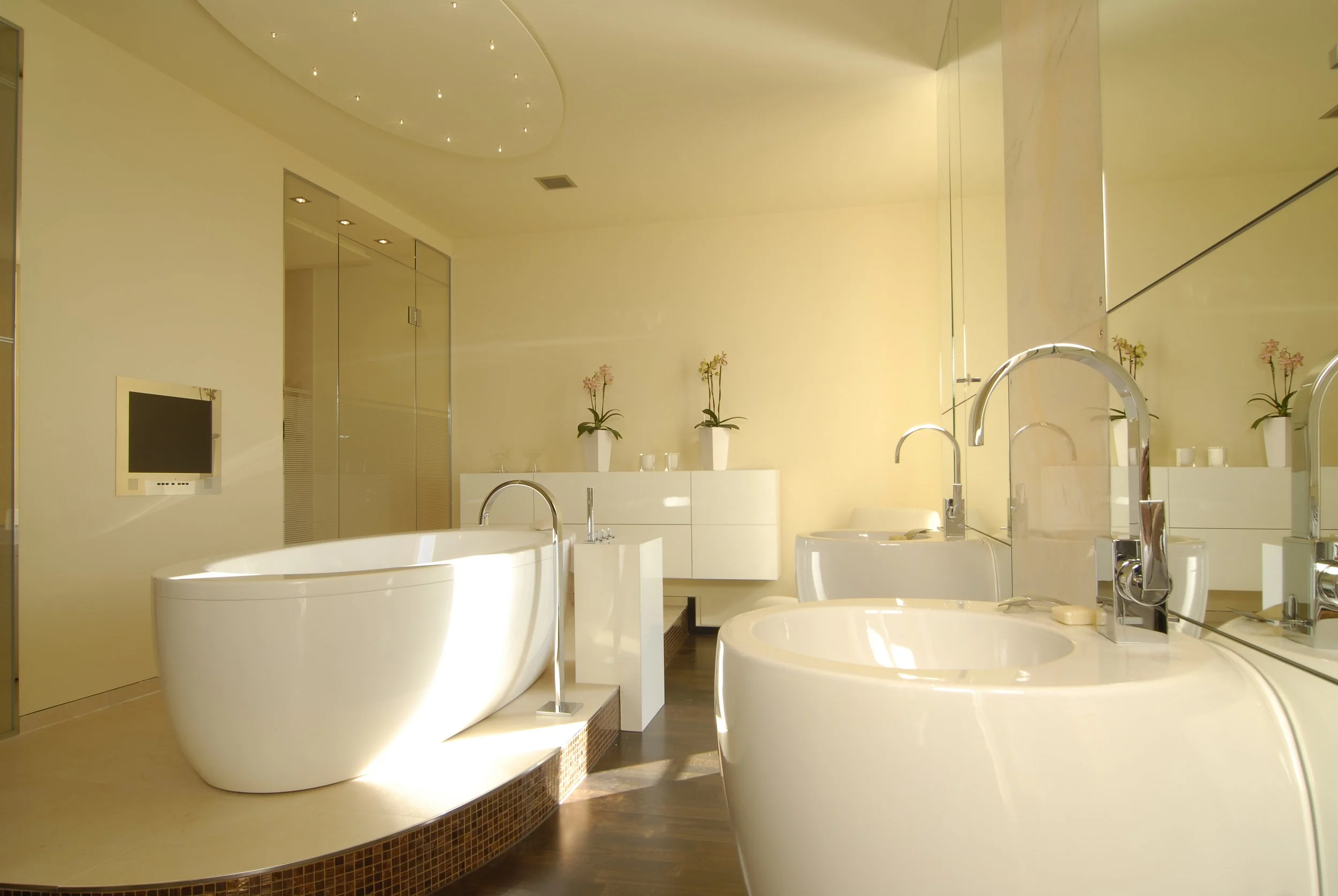 Helles, modernes Badezimmer mit weißer Badewanne, Waschbecken, Spiegel, Pflanzen und Dekorationen.