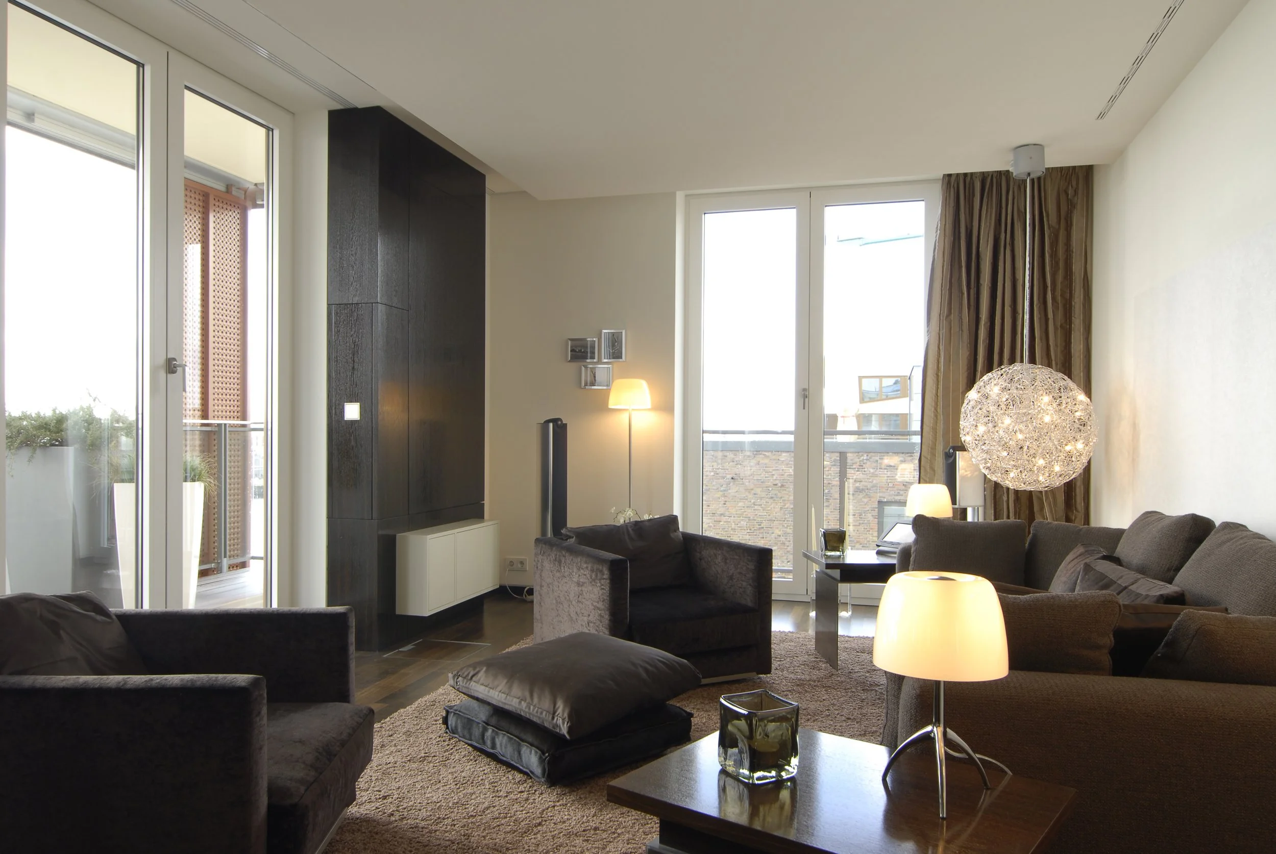 Gemütliches Wohnzimmer mit Sofas, Armchair, Stehlampen, Couchtisch, Kissen, großer Fensterfront und Balkonblick.