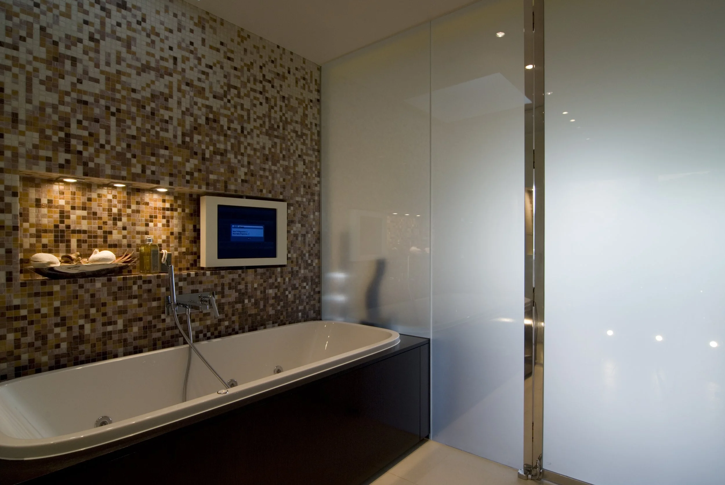 Modernes Badezimmer mit Badewanne, Mosaikwand, Spiegel und gläserner Trennwand.