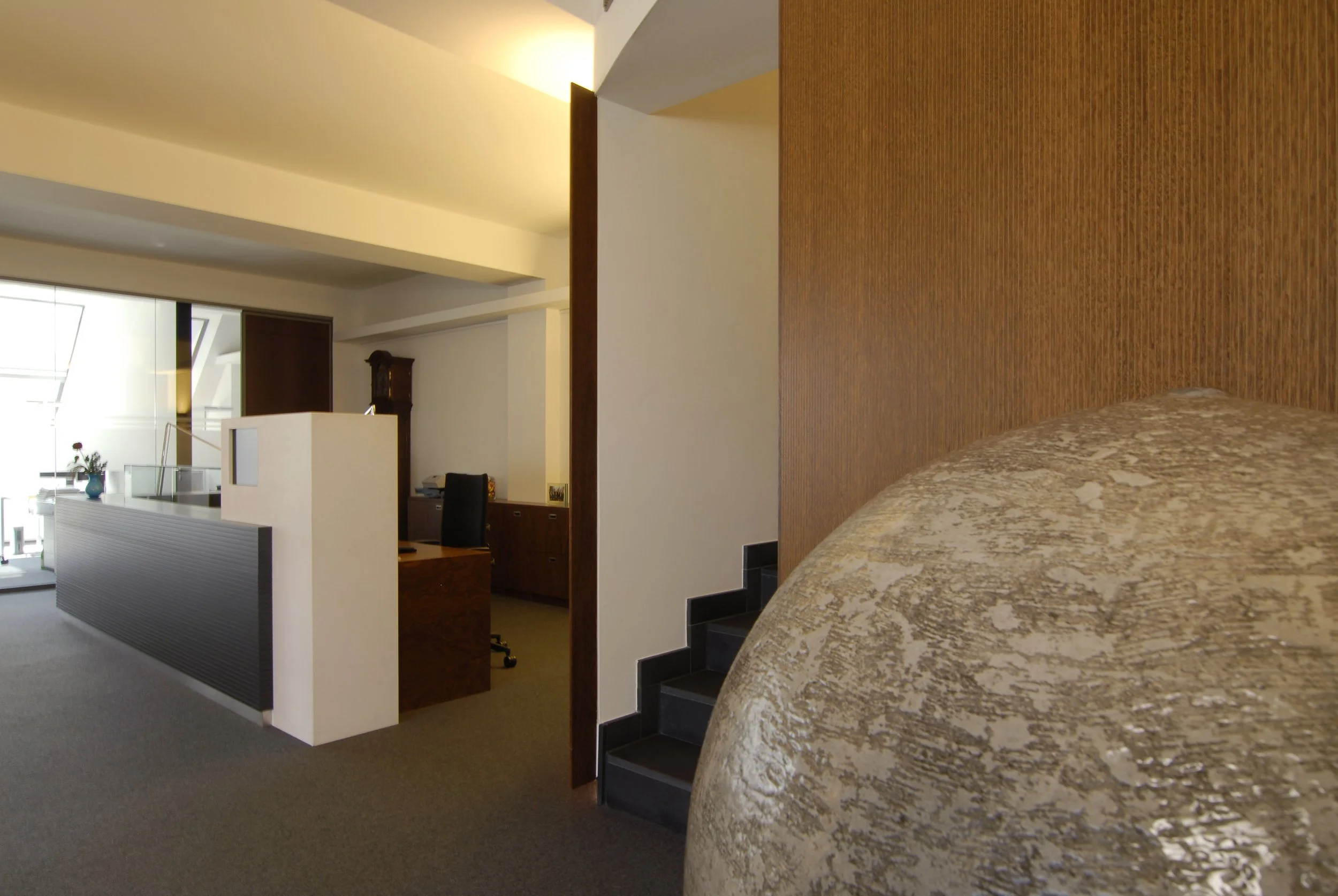 Innenaufnahme eines Wohn- oder Bürozimmers mit Schreibtisch, Stuhl, Möbeln, Treppe und Bett mit goldfarbenem Bezug.