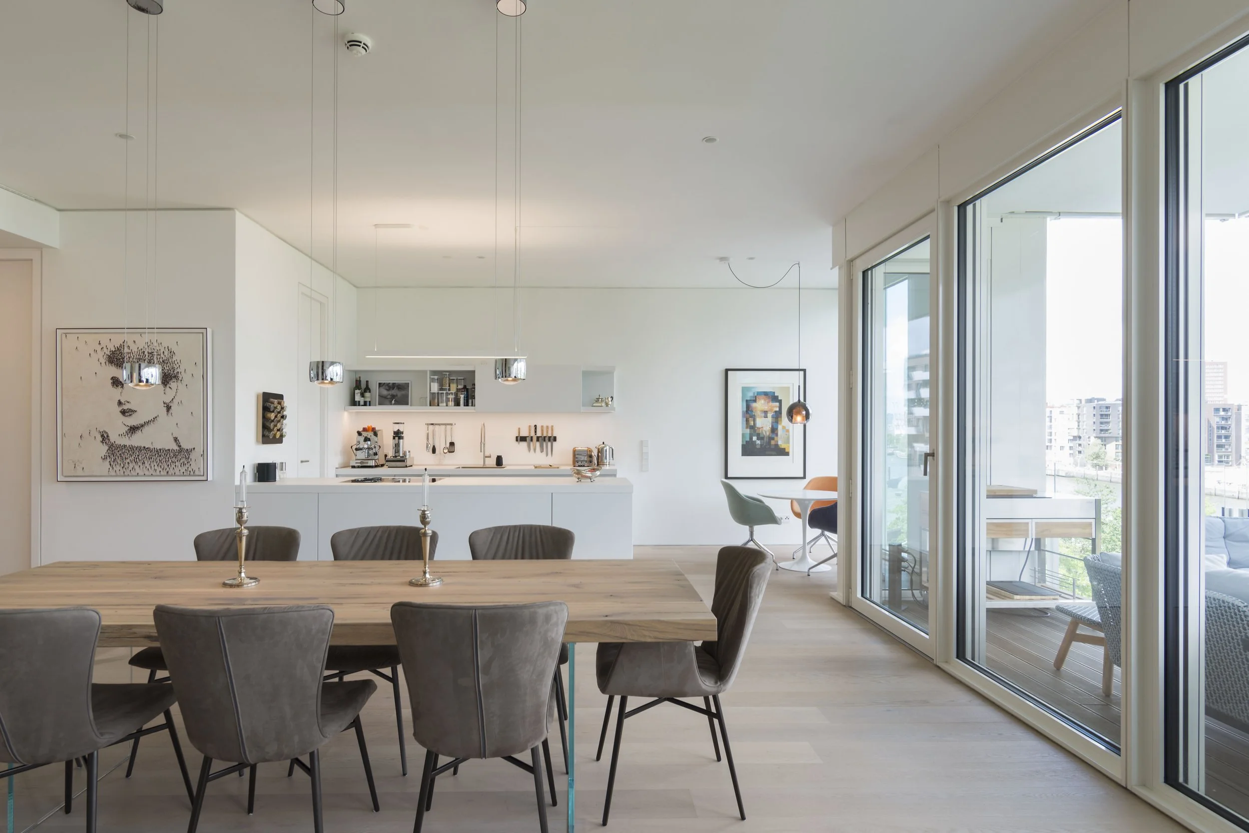 Offene, moderne Wohnküche und Essbereich in einem hellen, minimalistischen Apartment mit großem Esstisch und Blick auf den Balkon
