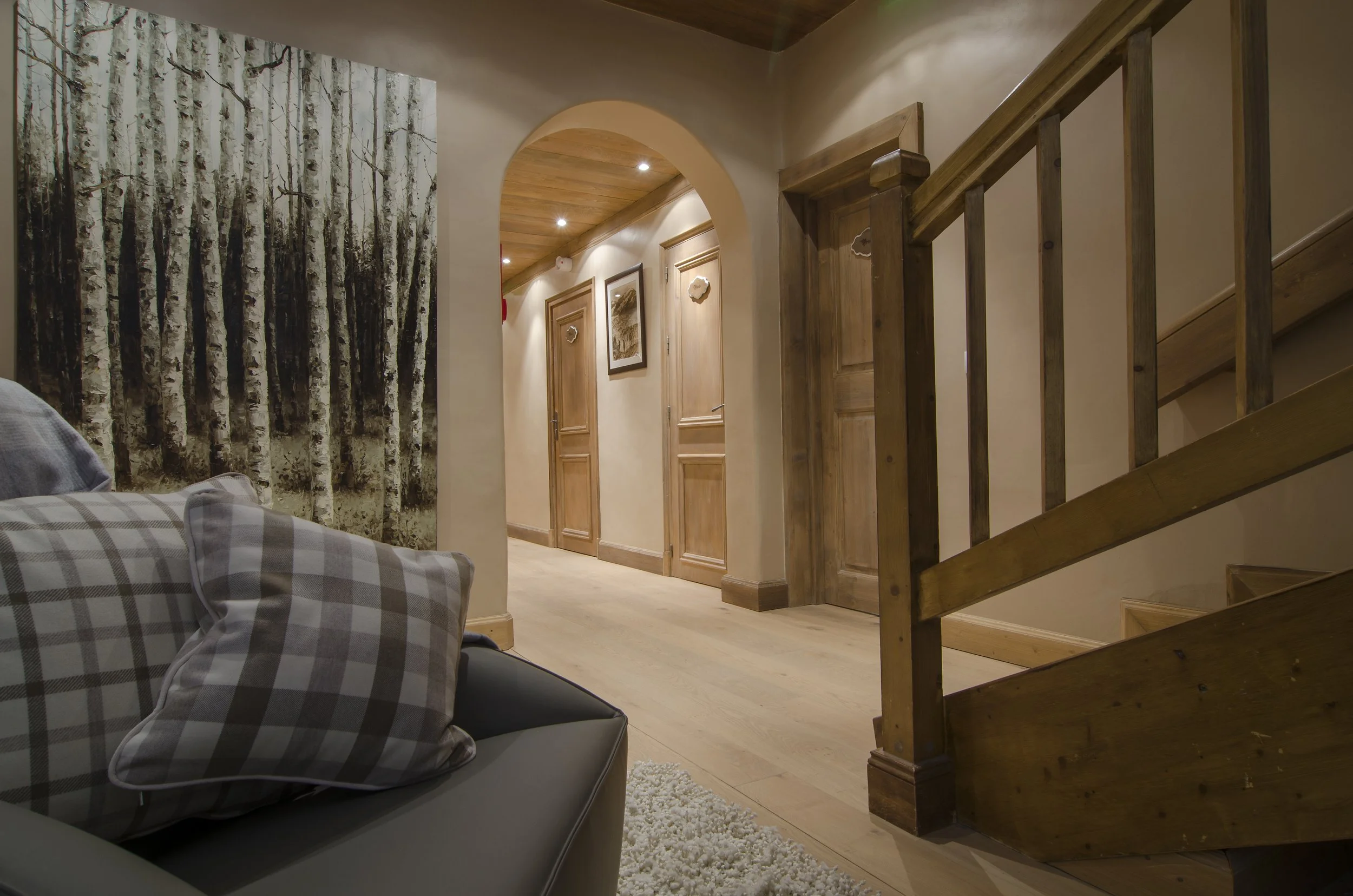 Wohnzimmer mit Kissen vor einem Wandbild eines Birkenwaldes, Holztüren im Flur, Holzstufen an der Treppe.