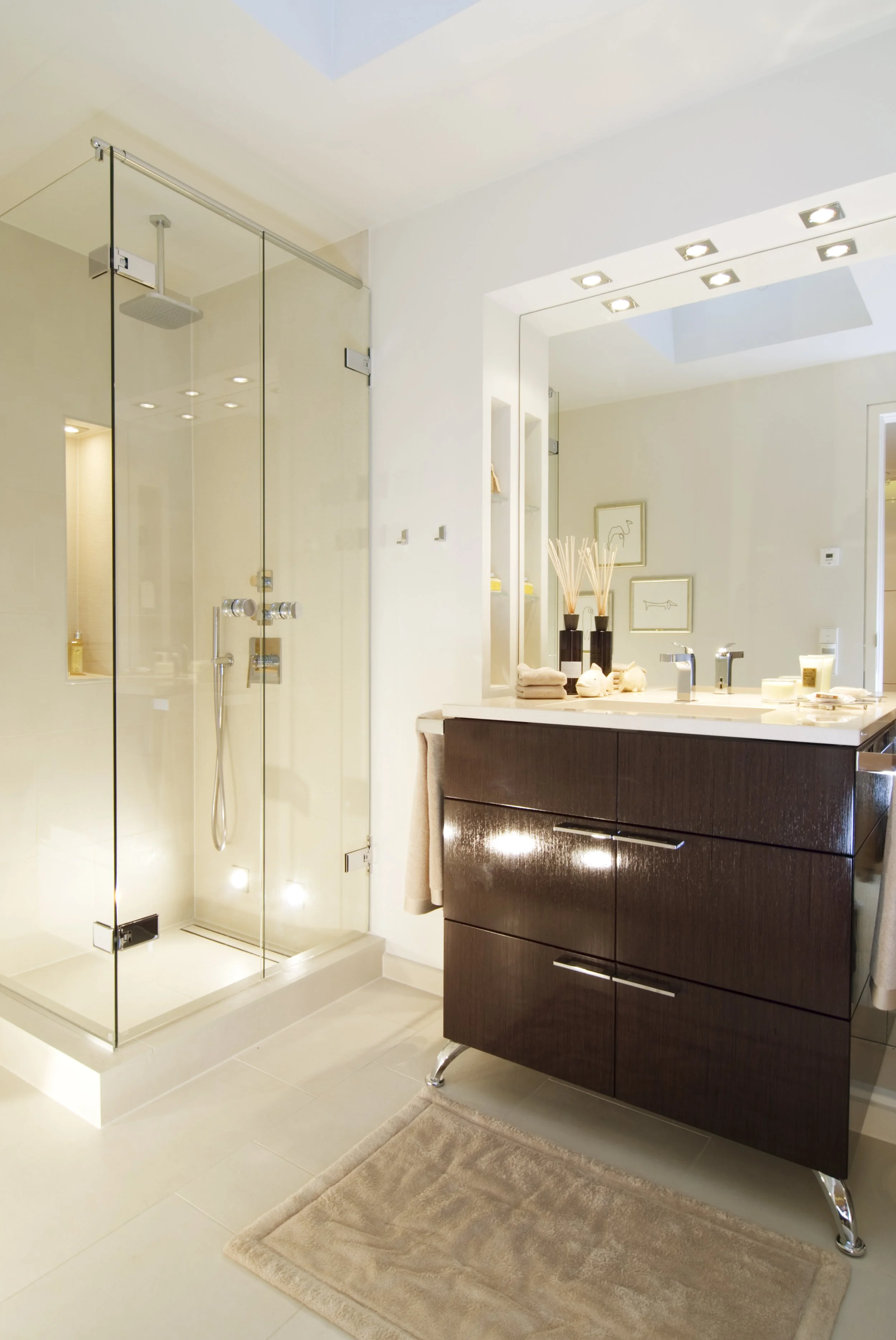 Modernes Badezimmer mit begehbarer Glas-Dusche, dunklem Waschtischuntrag, großen Spiegeln, dekorativen Accessoires und hellem Ambiente.