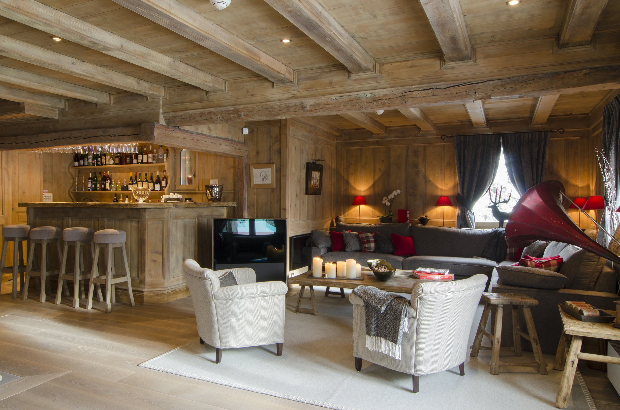 Gemütliches Wohnzimmer mit Holzpaneelen, Sofa, Armlehnstühlen, Kamin, Kamin-Ofen, Dekorationen, Kerzen und Bar im Hintergrund.