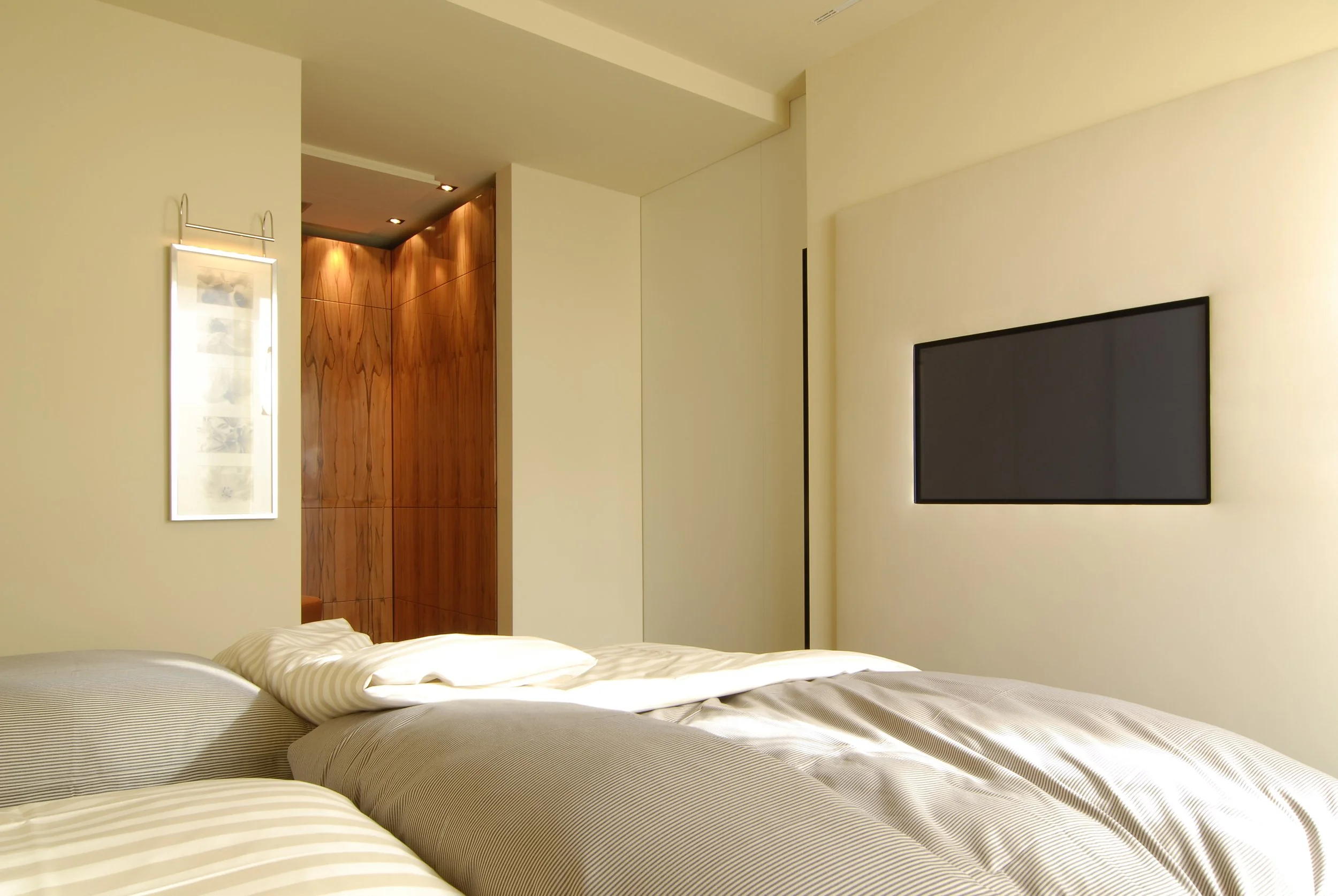 Ein modernes Schlafzimmer mit einem Bett, einem Fernseher an der Wand, einem Wandbild und einer Holzverkleidung im Hintergrund