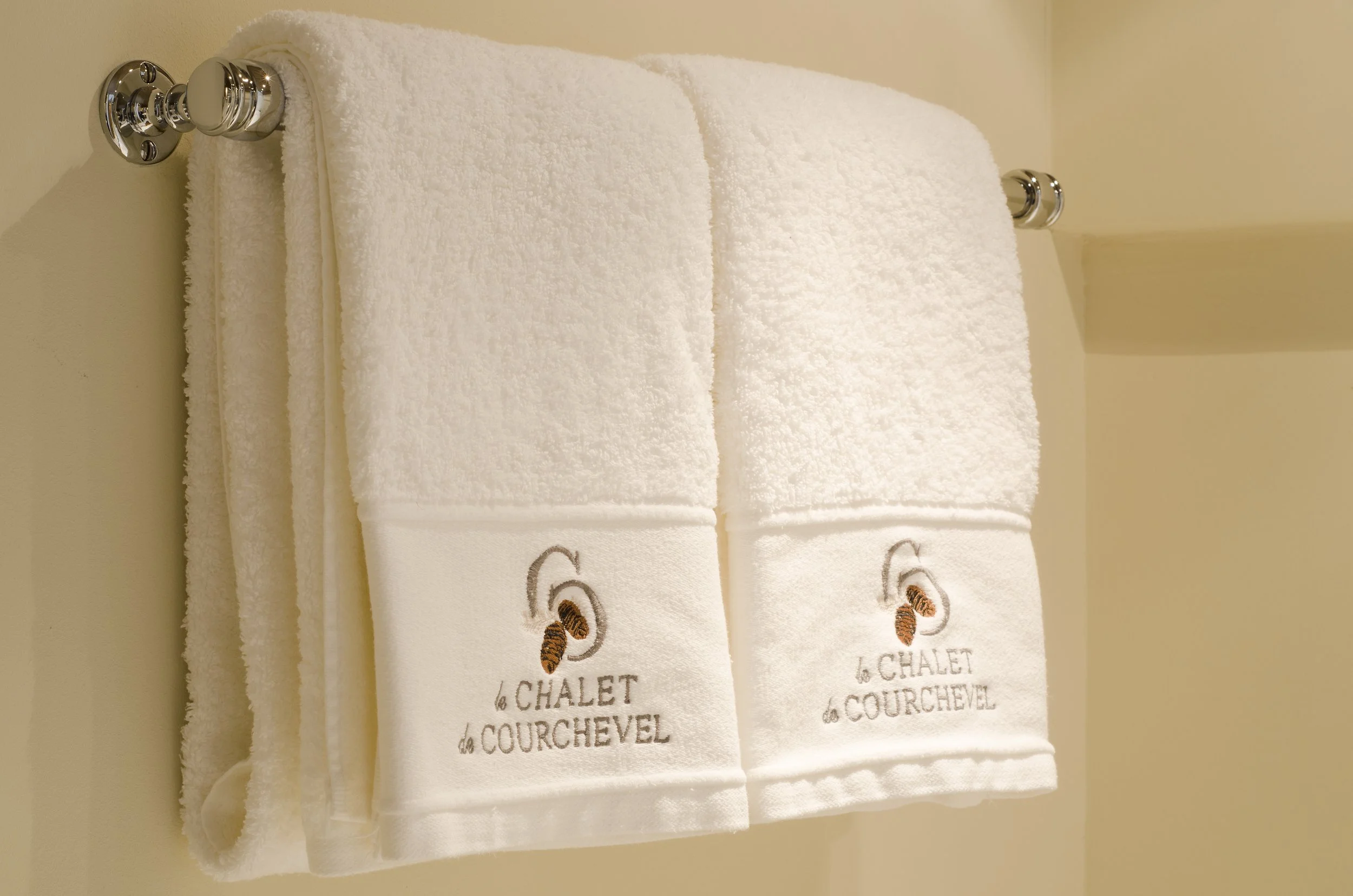 Zwei weiße Handtücher mit Stickerei, die einen Orangenzweig und den Text „le CHALET COURCHEVEL“ zeigen, hängen an einer Wand im Badezimmer.