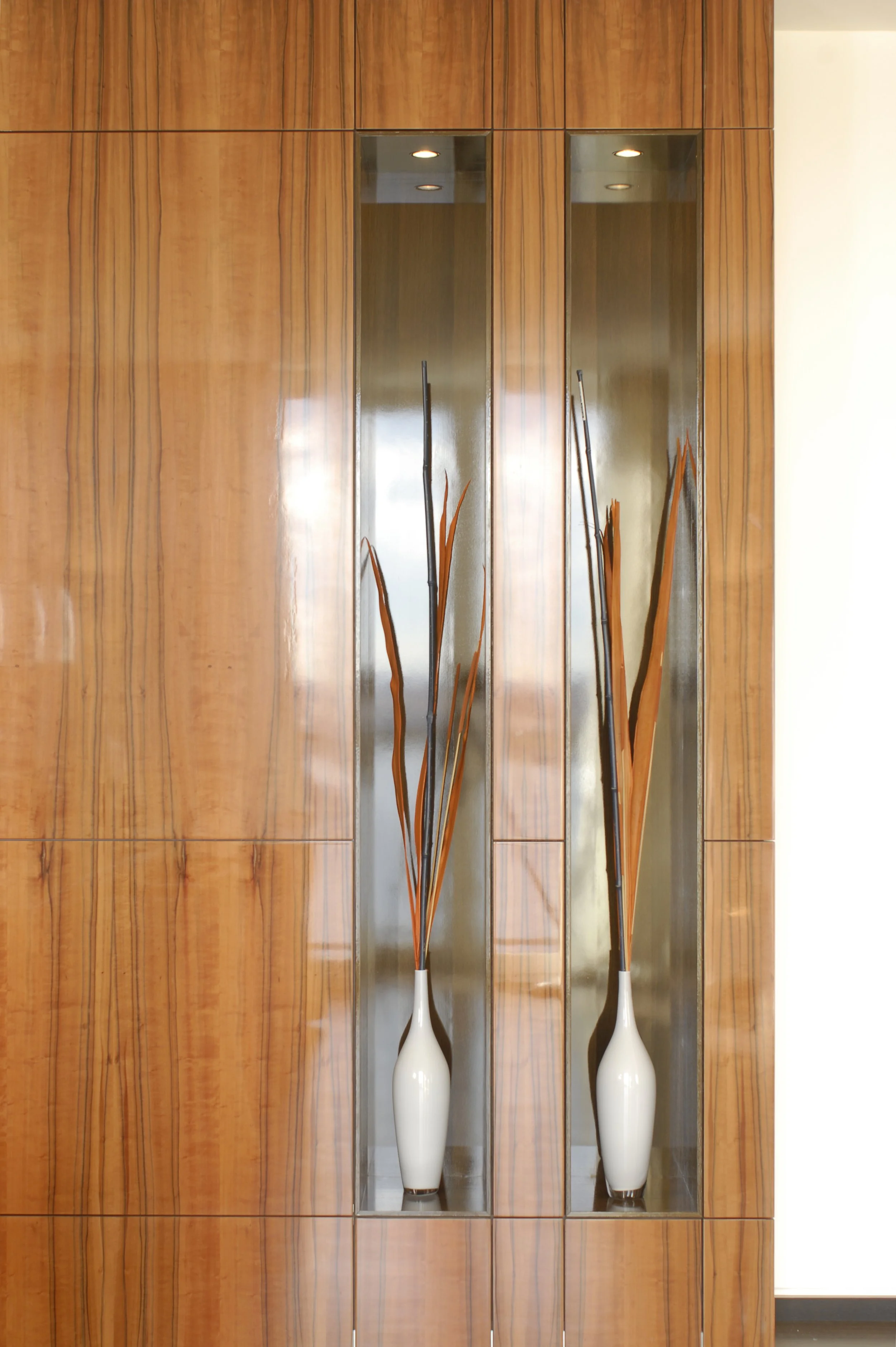 Zwei weiße Vasen mit trockenen Zweigen, in einer vertieften Holz- und Metallnische an einer Wand
