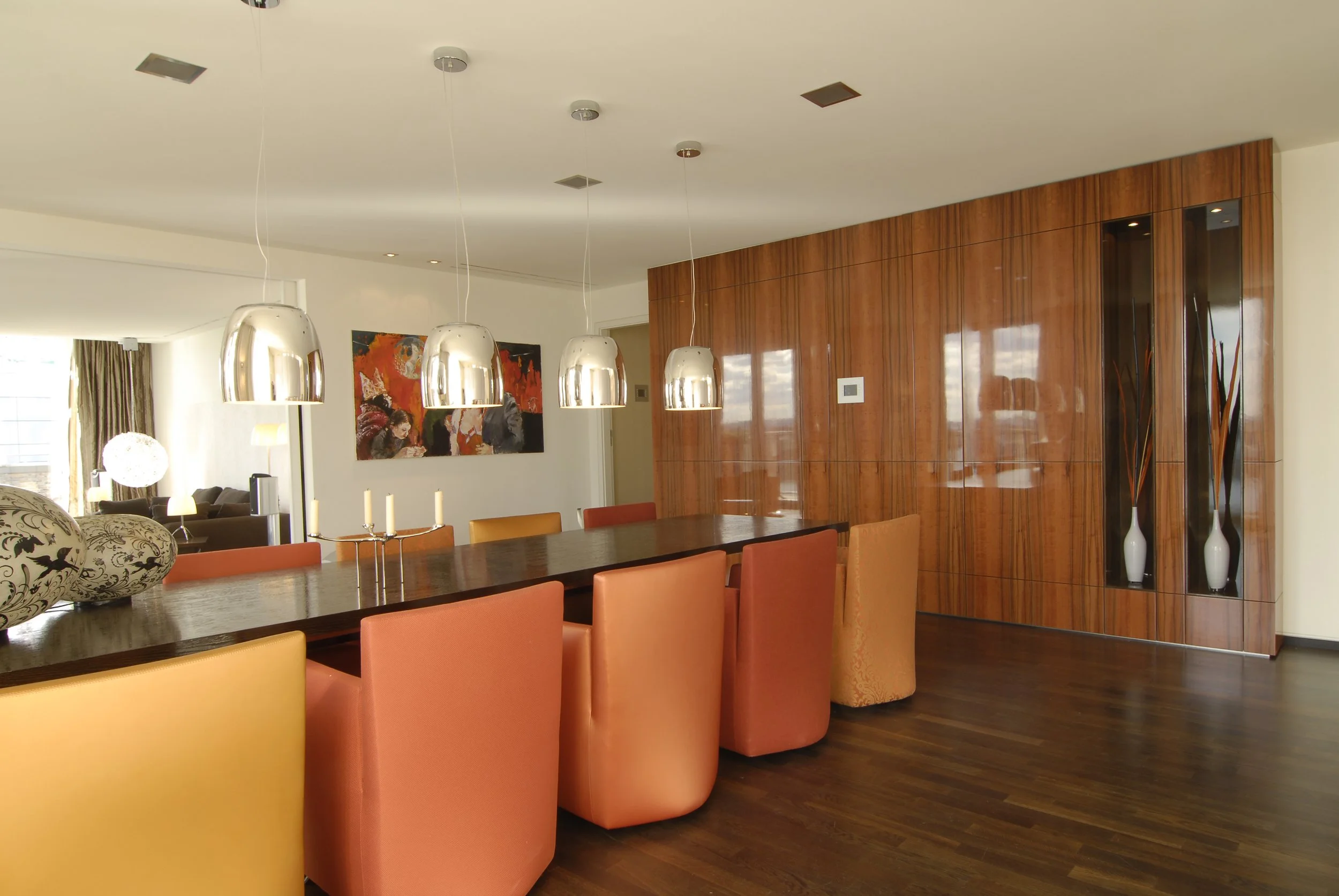 Esszimmer mit dunklem Holztisch, bunten Stühlen, modernen Lampen und Wanddekoration