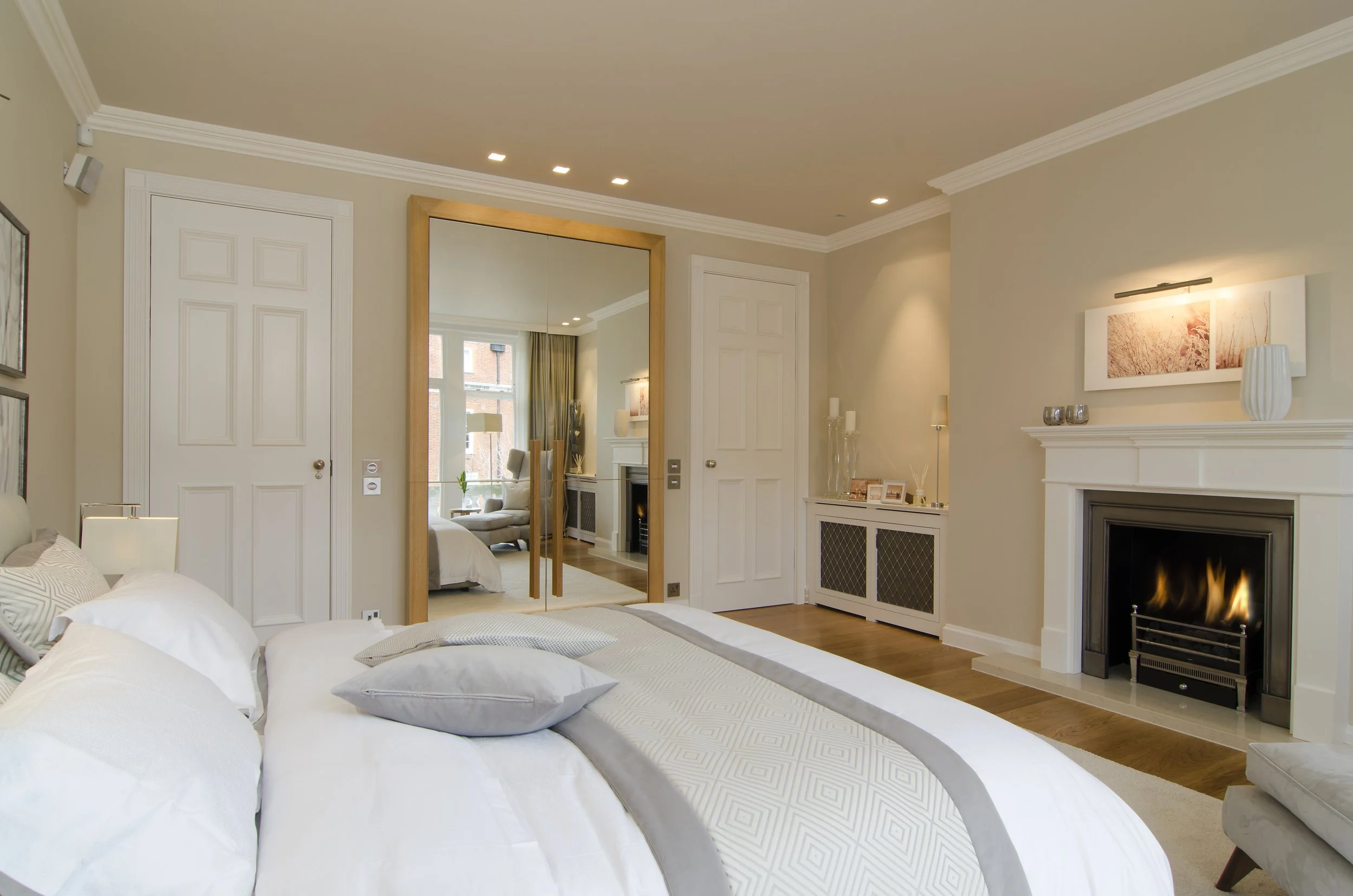 Ein gemütliches Schlafzimmer mit einem weißen Bett, einem Kamin, einer großen Garderobe mit Spiegel, einem schwarzen Kamin, passenden Vorhängen und moderner Dekoration.