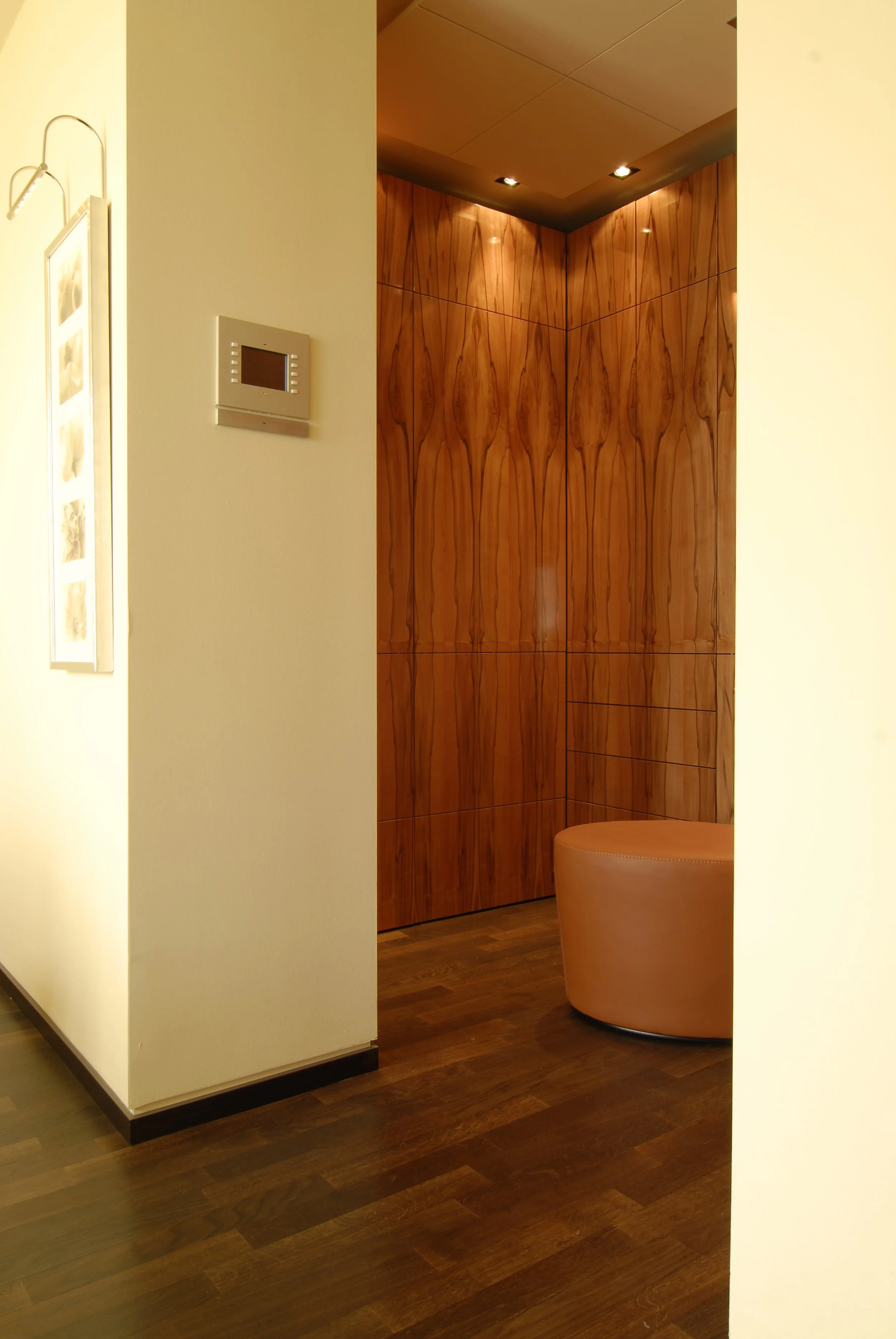 Der Blick in eine Ecke eines Raumes mit Holzvertäfelung, einer runden Bank und weichen Lichtquellen an der Decke.