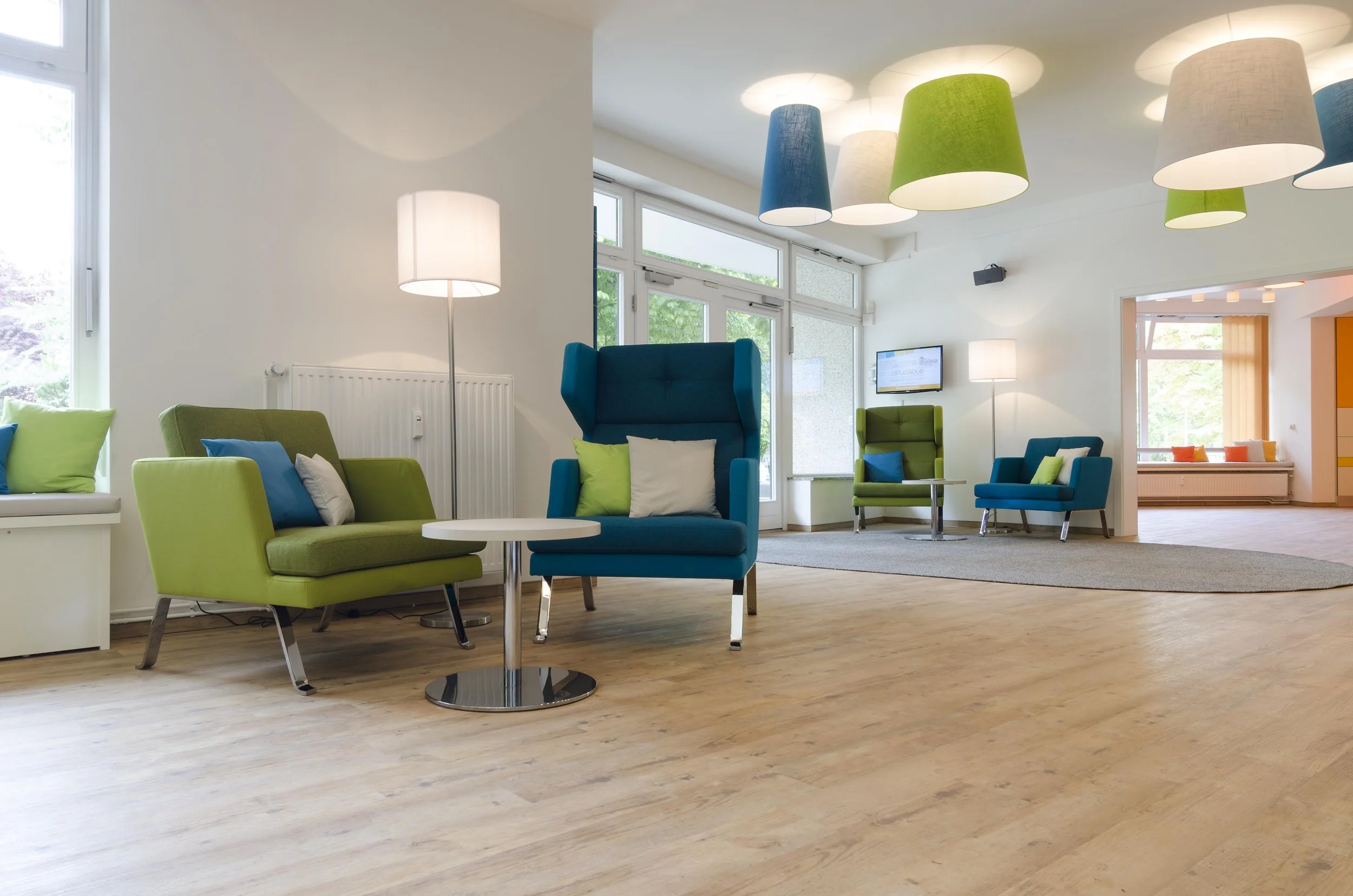 Modernes Wartezimmer mit bunten Sesseln, Sesselschirmen und Deckenleuchten in verschiedenen Farben