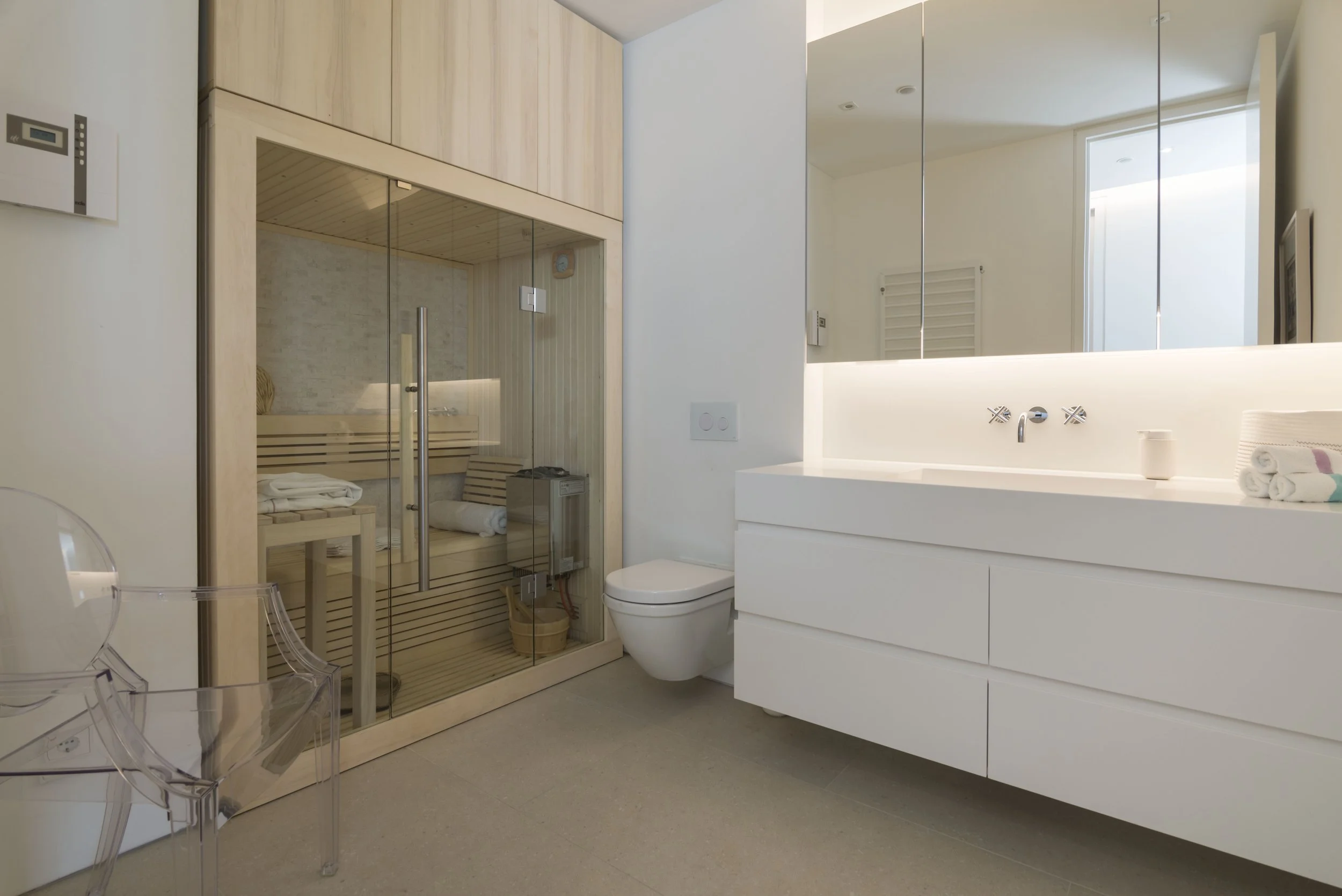 Modernes Badezimmer mit begehbarer Sauna, weißem Waschtisch und großem Spiegel.