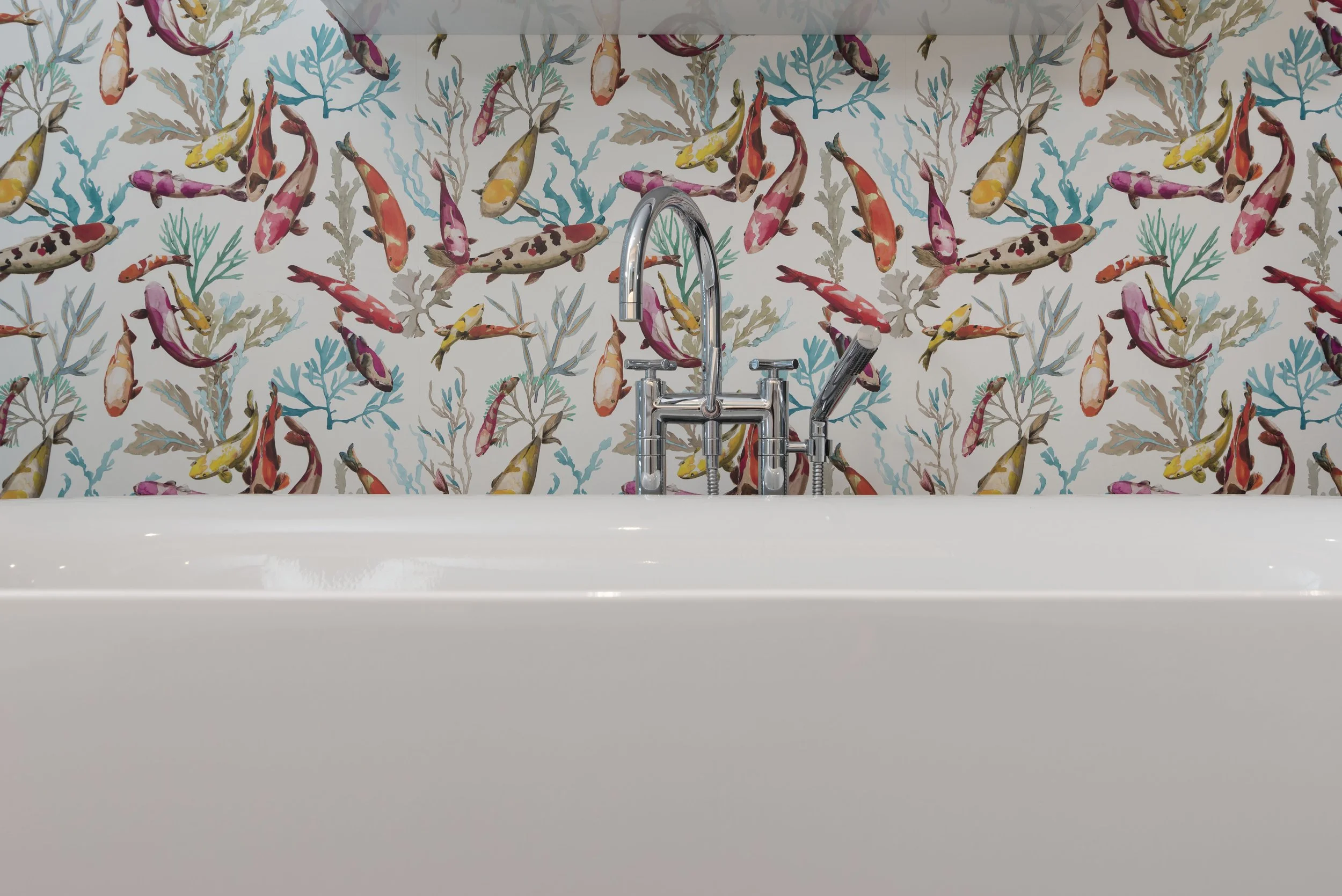 Waschbecken mit Wasserhahn vor einer bemalten Fliesenwand mit bunten Fisch- und Korallenmotiv.
