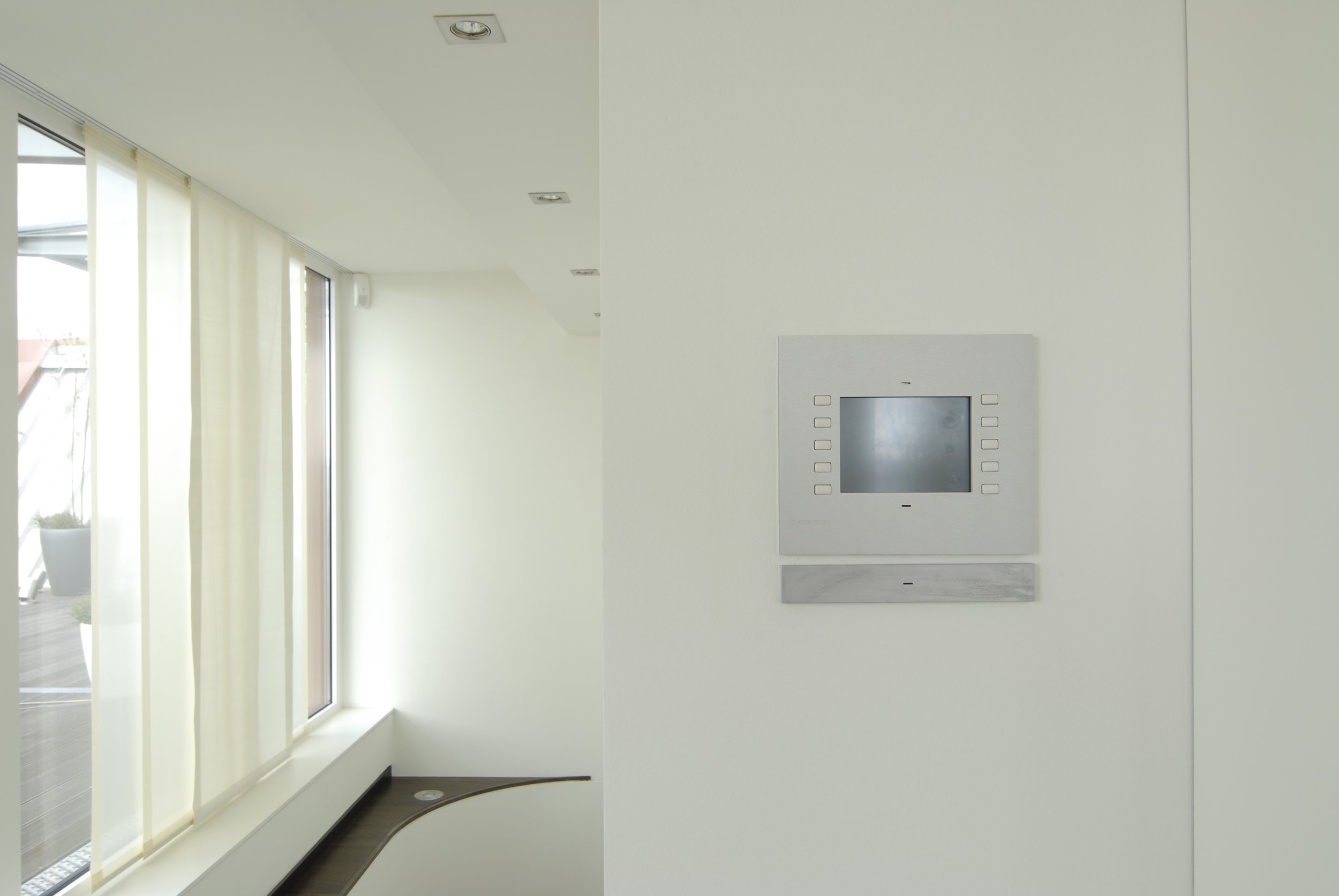 Innenansicht eines modernen Hauses mit großen Fenstern, weißen Wänden und einem Monitor an der Wand.