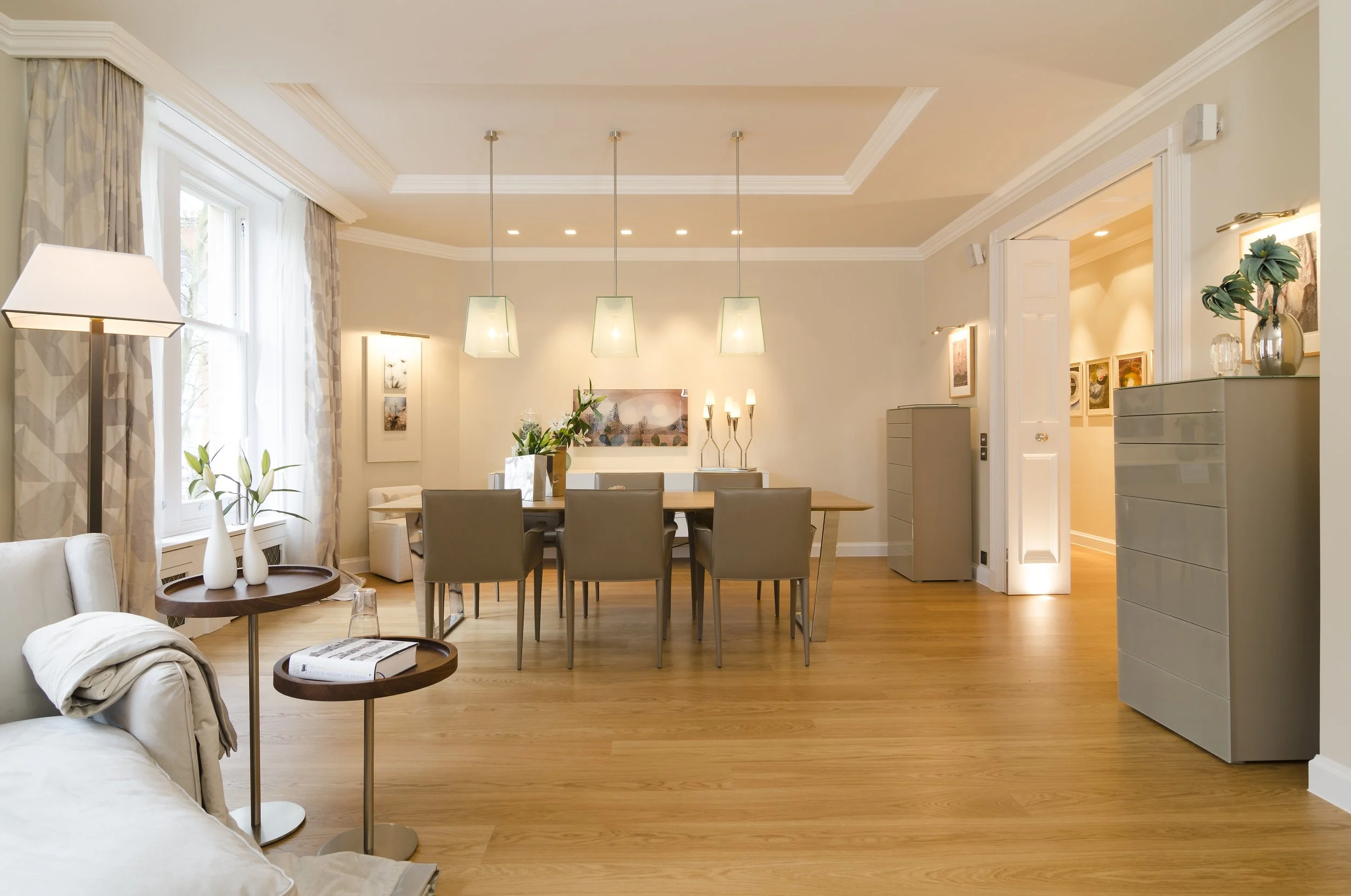 Helles Wohnzimmer mit Essbereich, beigen Möbeln, Holzfußboden, großen Fenstern und moderner Dekoration.