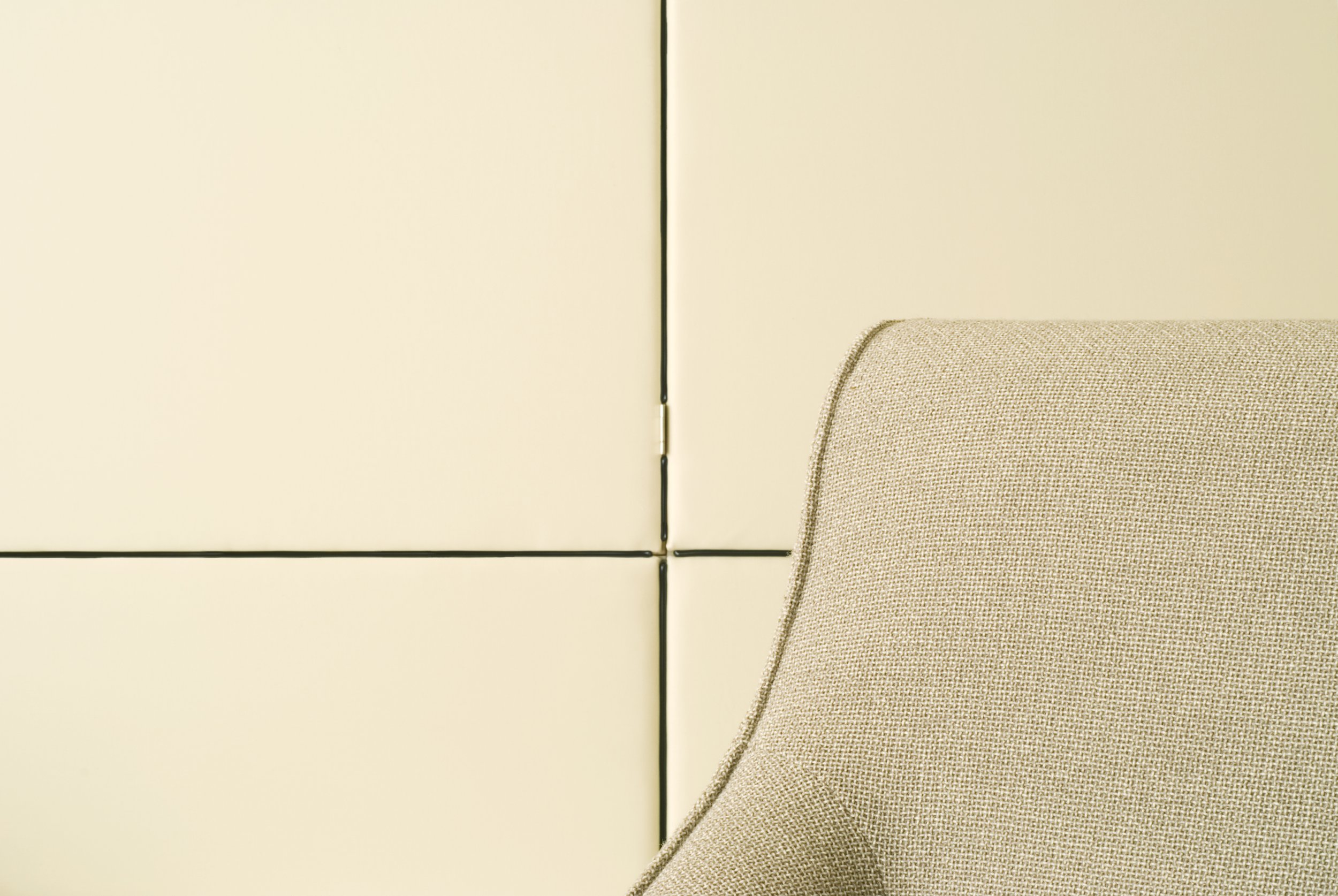 Nahaufnahme einer beige Polsterecke neben weißen Schranktüren mit schwarzen Nähten.