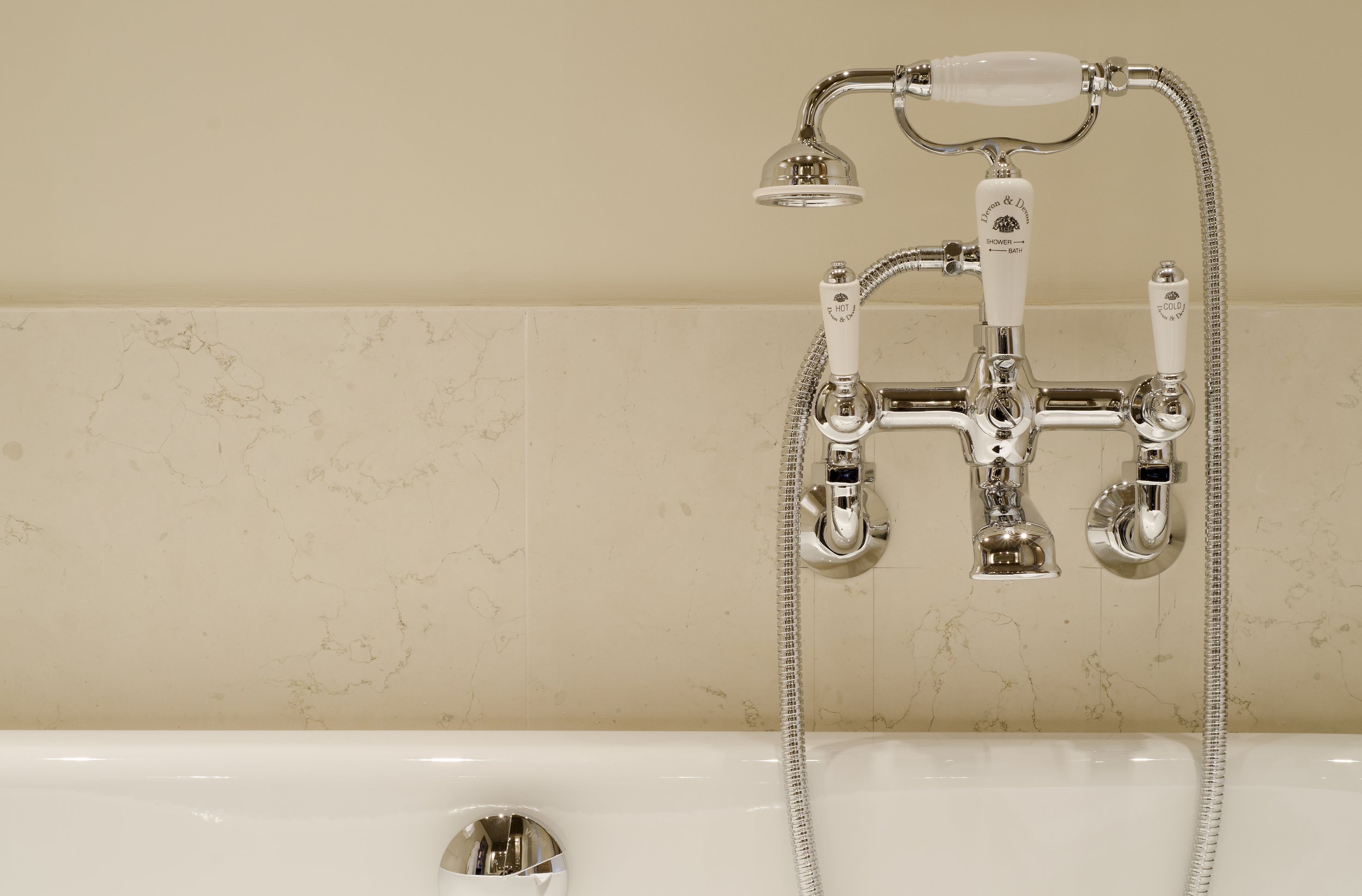 Nahaufnahme eines Badewannenarmatur mit mehreren Wasserhähnen, einer Brause und weißen Griffen, beschriftet mit 'HOT', 'COLD' und 'SHOWER & BATH'.