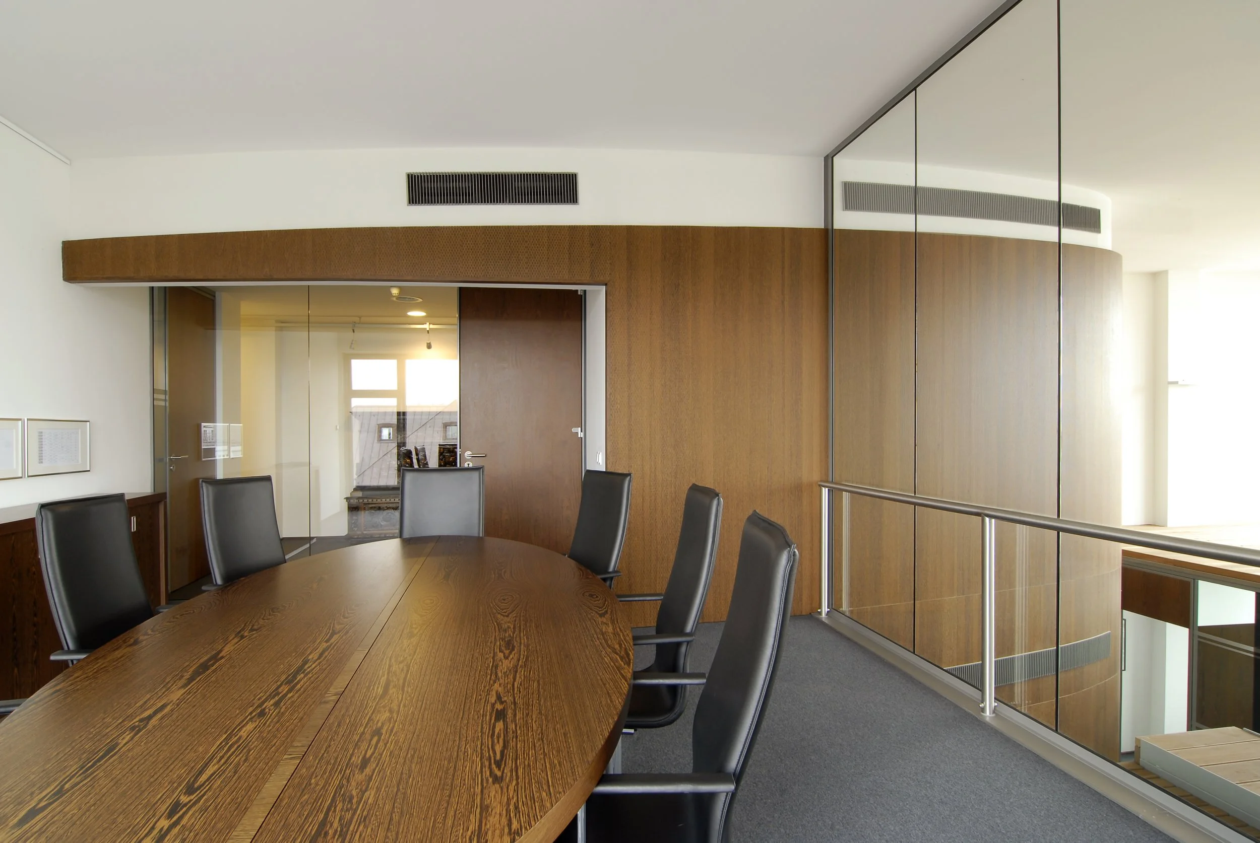 Besprechungsraum mit Holztablett, schwarzen Stühlen und Glaswänden in einem modernen Bürogebäude.