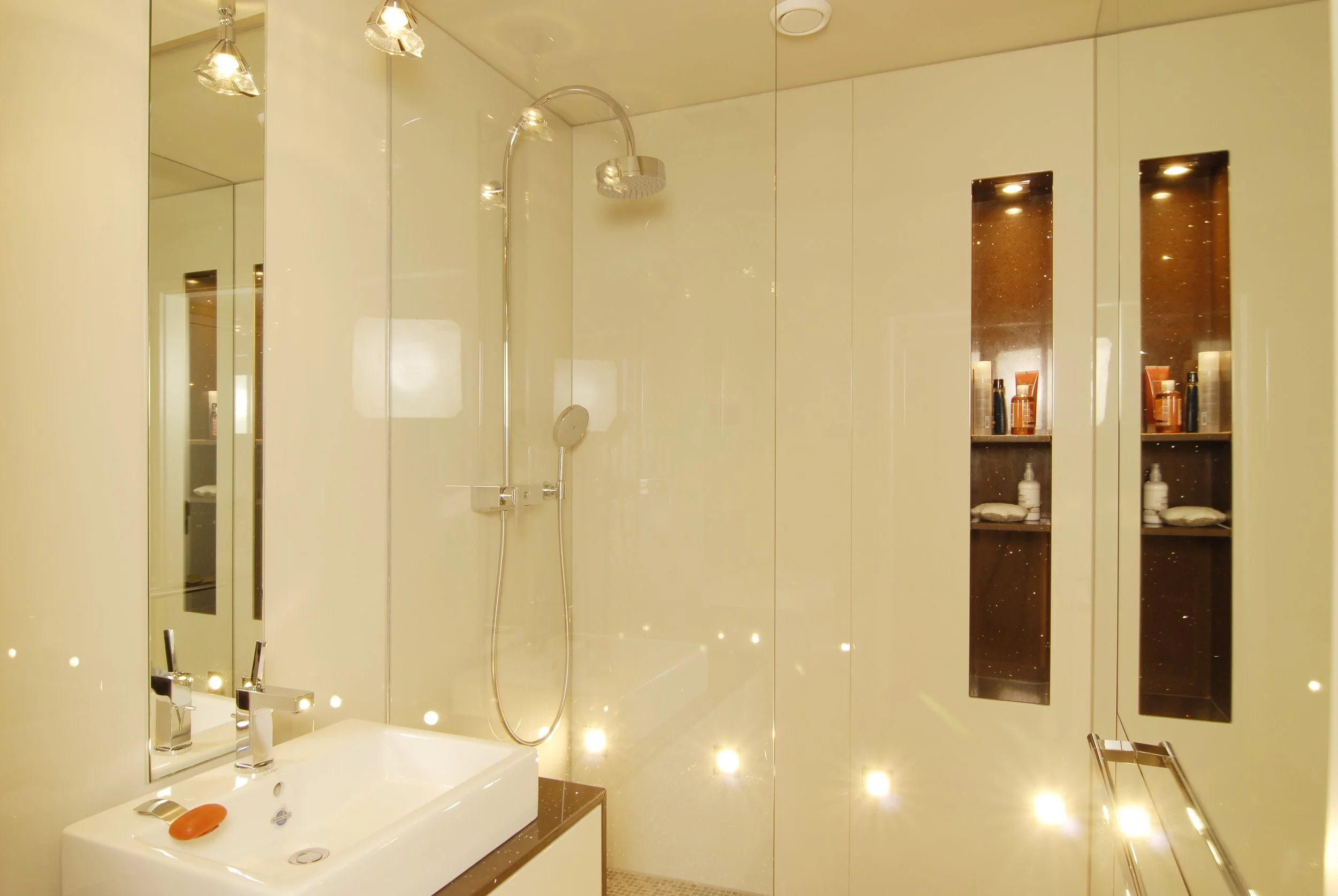 Modernes Badezimmer mit Spiegel, Waschbecken, Dusche und integrierten Regalen mit Pflegeprodukten.